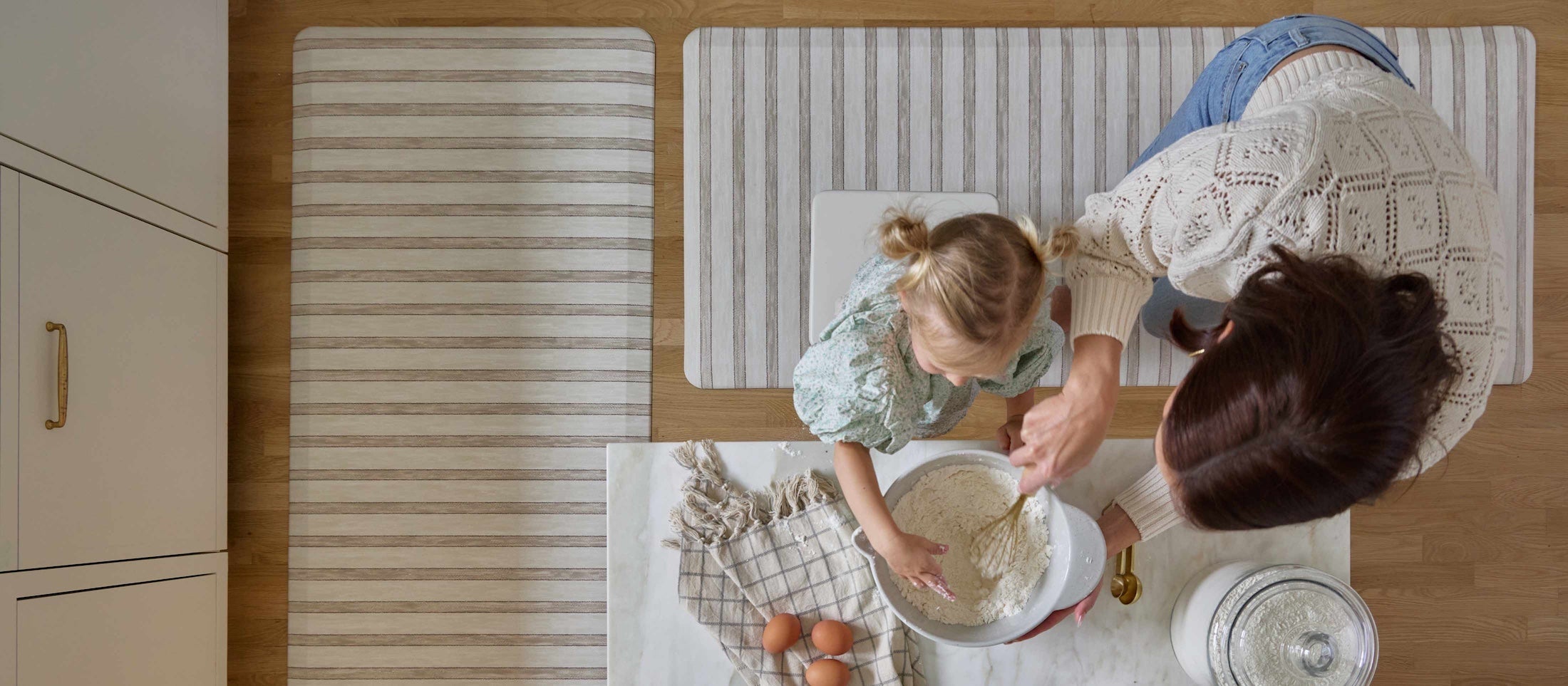 Overhead shot of woman standing on the Ula windmill blue and white boho print standing mat at the kitchen counter cutting a piece of bread
