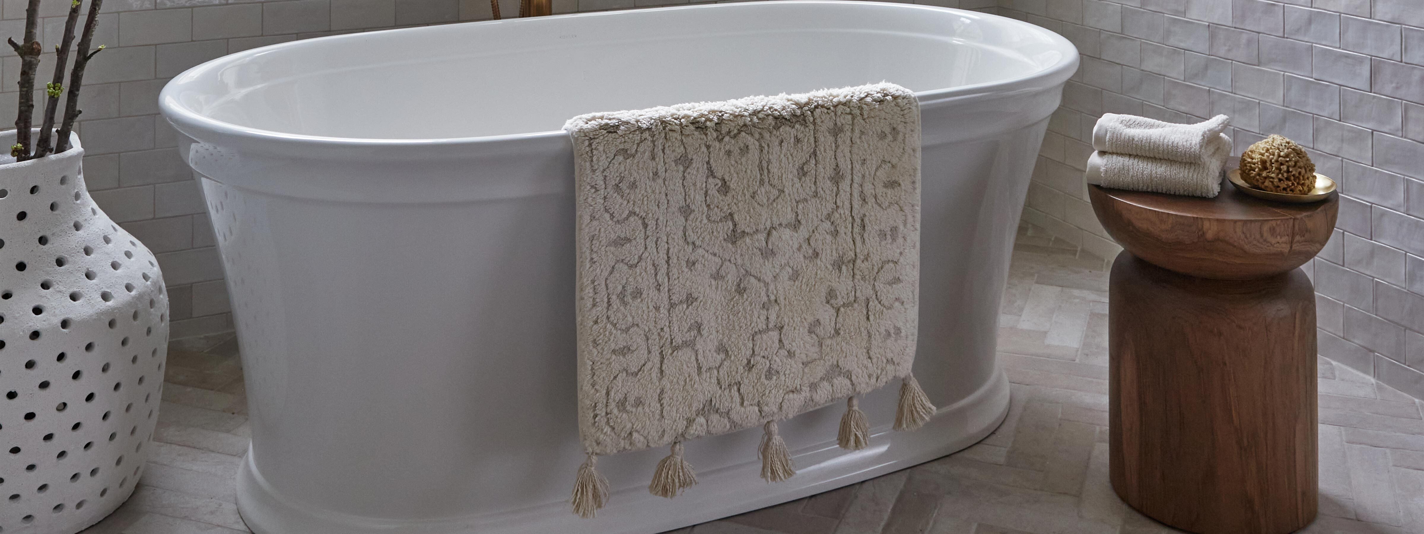 Arden pearl cream and white persian rug pattern bath mat shown hanging over the edge of a bath tub