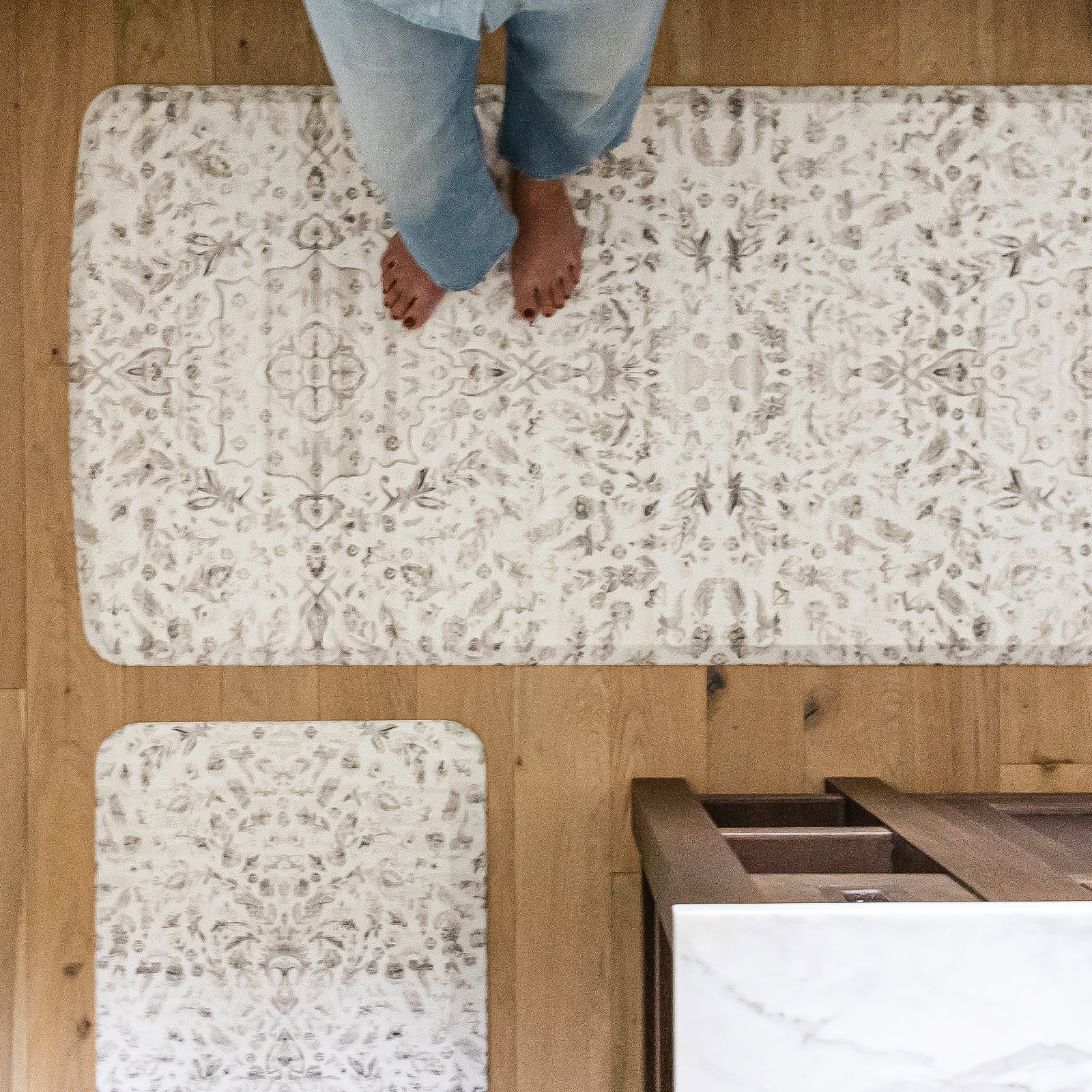 Emile latte beige and gray floral boho kitchen mat shown from above in kitchen with woman's feet standing on size 30x108
