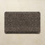A rectangular kitchen mat with rounded corners featuring an intricate, faded damask-style floral pattern in dark brown and charcoal gray, displayed on a textured beige background.