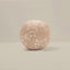 A round, upholstered cushion or pouf in a dusty blush pink fabric with a white floral pattern, set against a neutral beige background.
