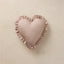 A heart-shaped decorative pillow in a dusty rose pink fabric with a small white polka-dot pattern and a ruffled satin border, displayed on a neutral beige textured background.