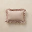 A rectangular throw pillow in a dusty rose velvet fabric with a white polka-dot pattern and ruffled trim, displayed on a neutral beige textured background.