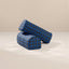 Two cylindrical armrest pillows with a blue and black grid plaid pattern, stacked on a light beige surface against a matching beige background.