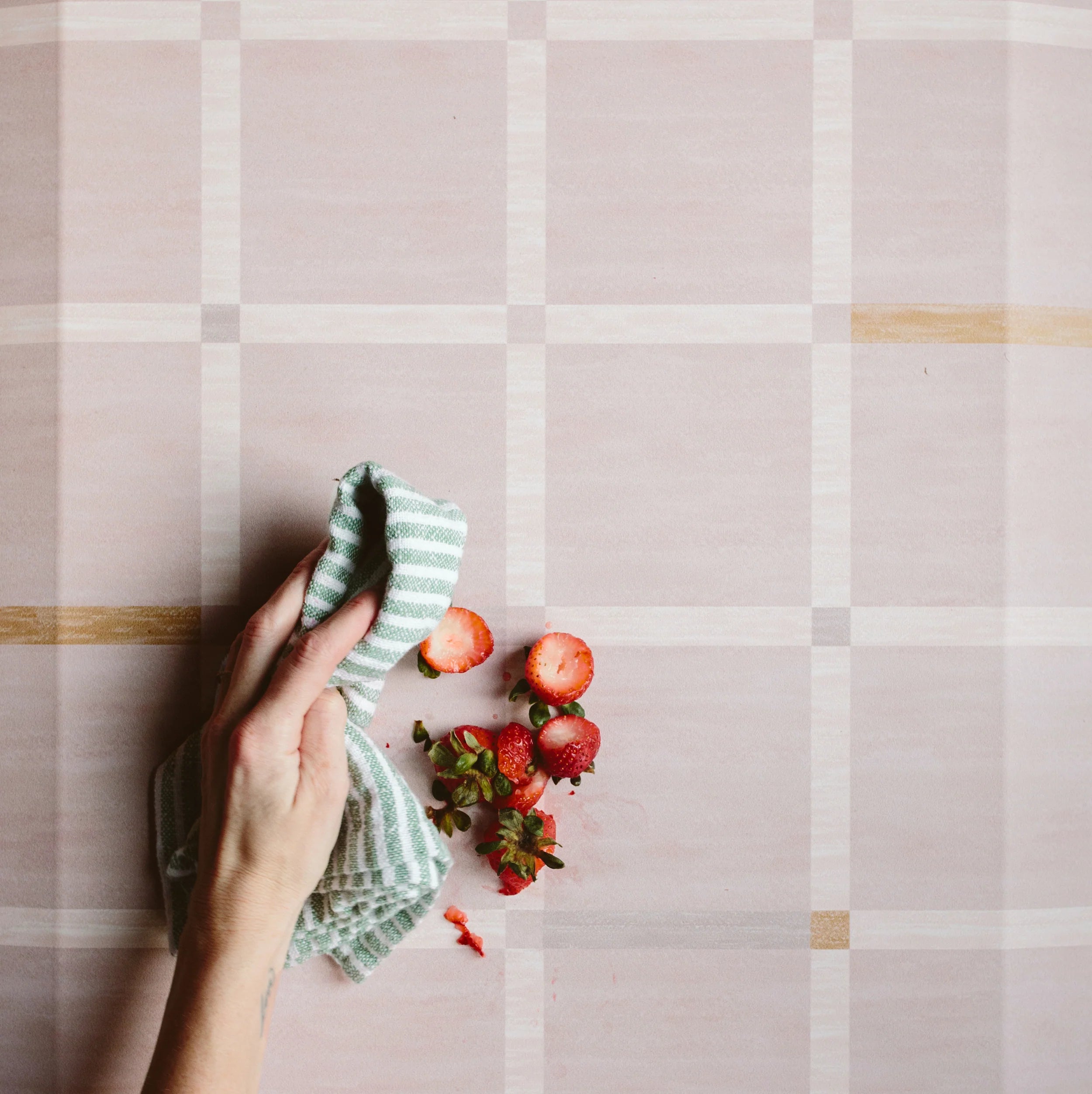 Windowpane blush pink and white grid pattern standing mat. Shown with woman's hand wiping up a spill