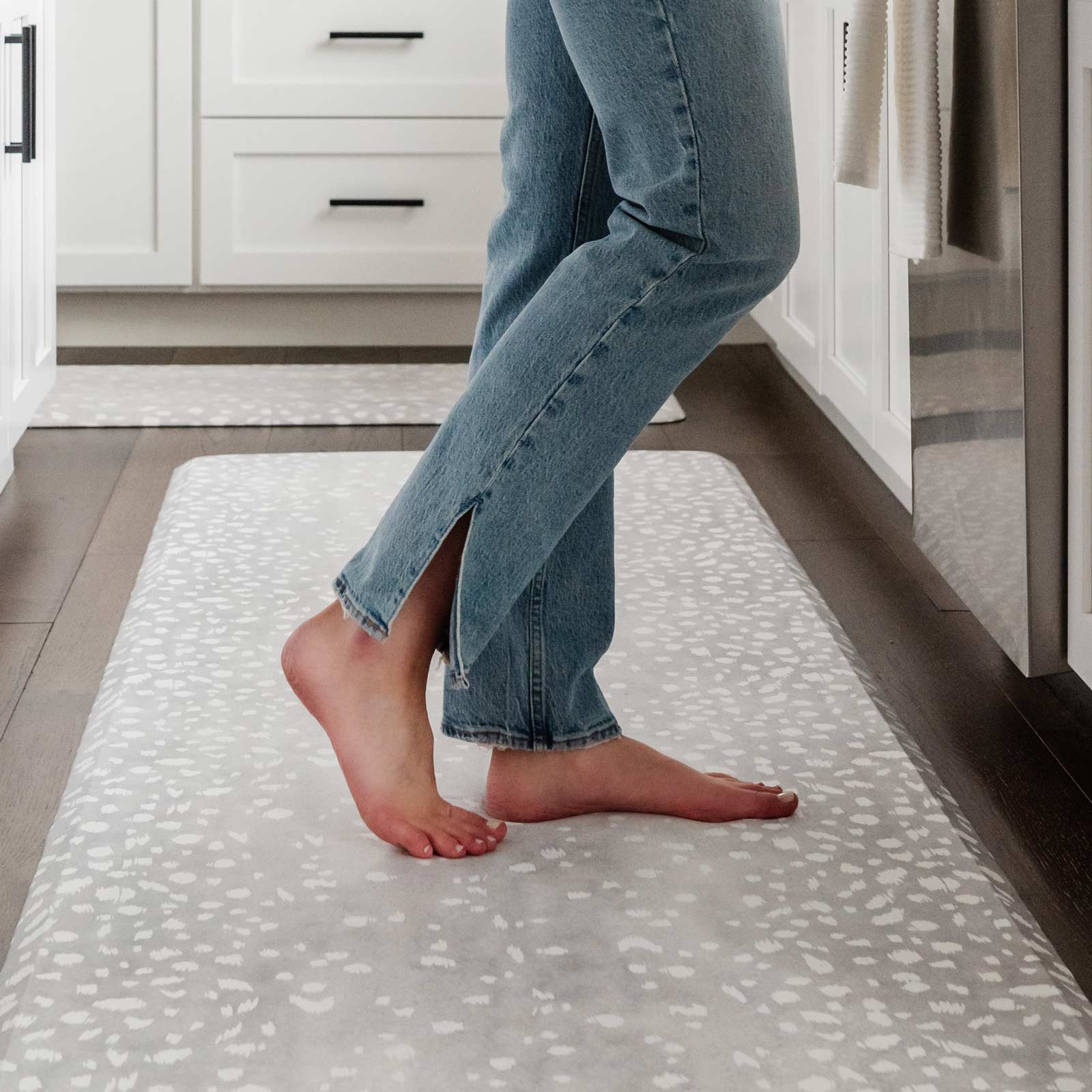 Fawn silver gray animal print kitchen mat shown in size 30x108 in front of kitchen counter with woman's feet standing on the mat
