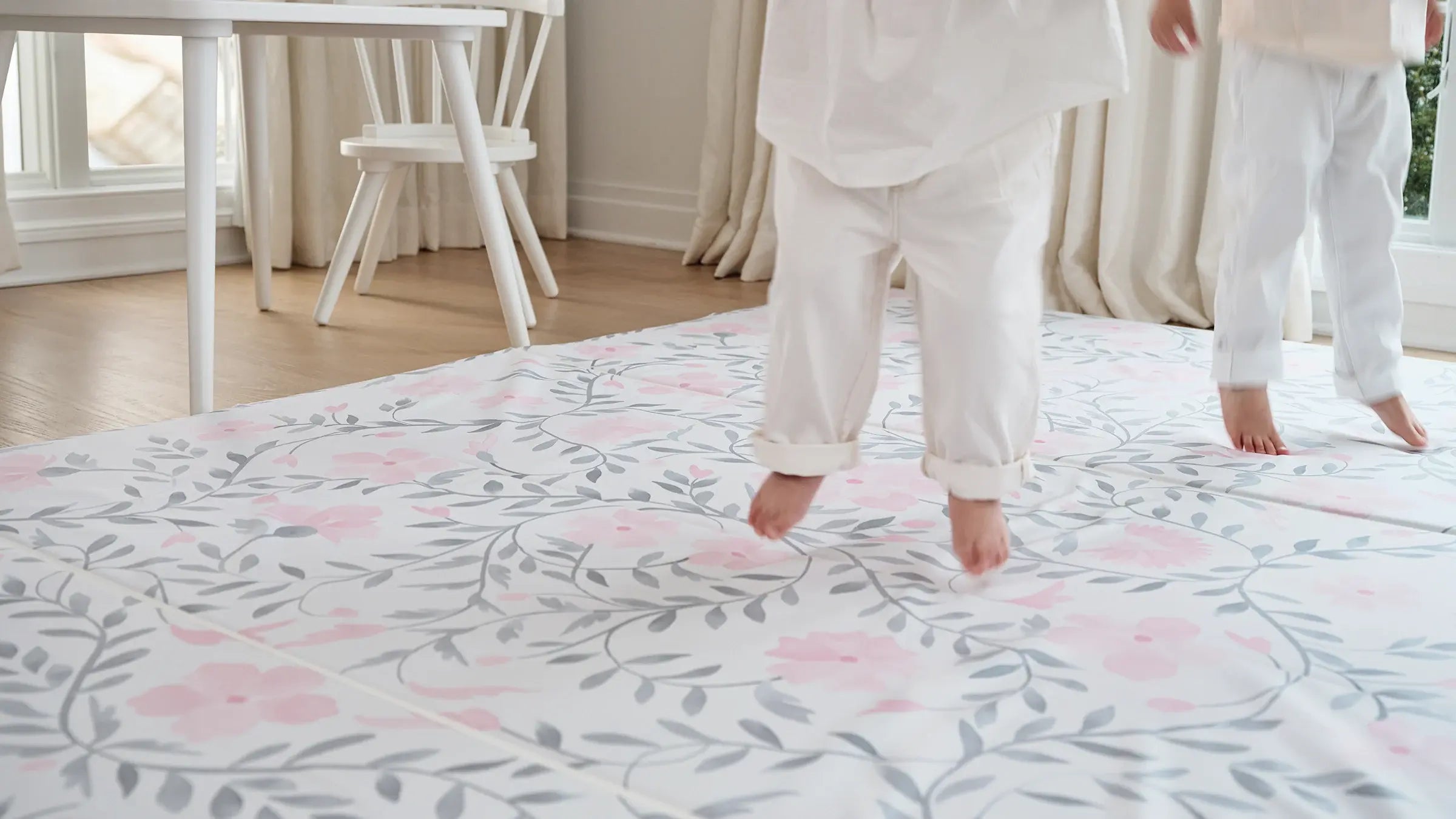 Faye Macaron gray and pink floral tumbling mat shown in play room with 2 toddlers feet jumping up off the mat