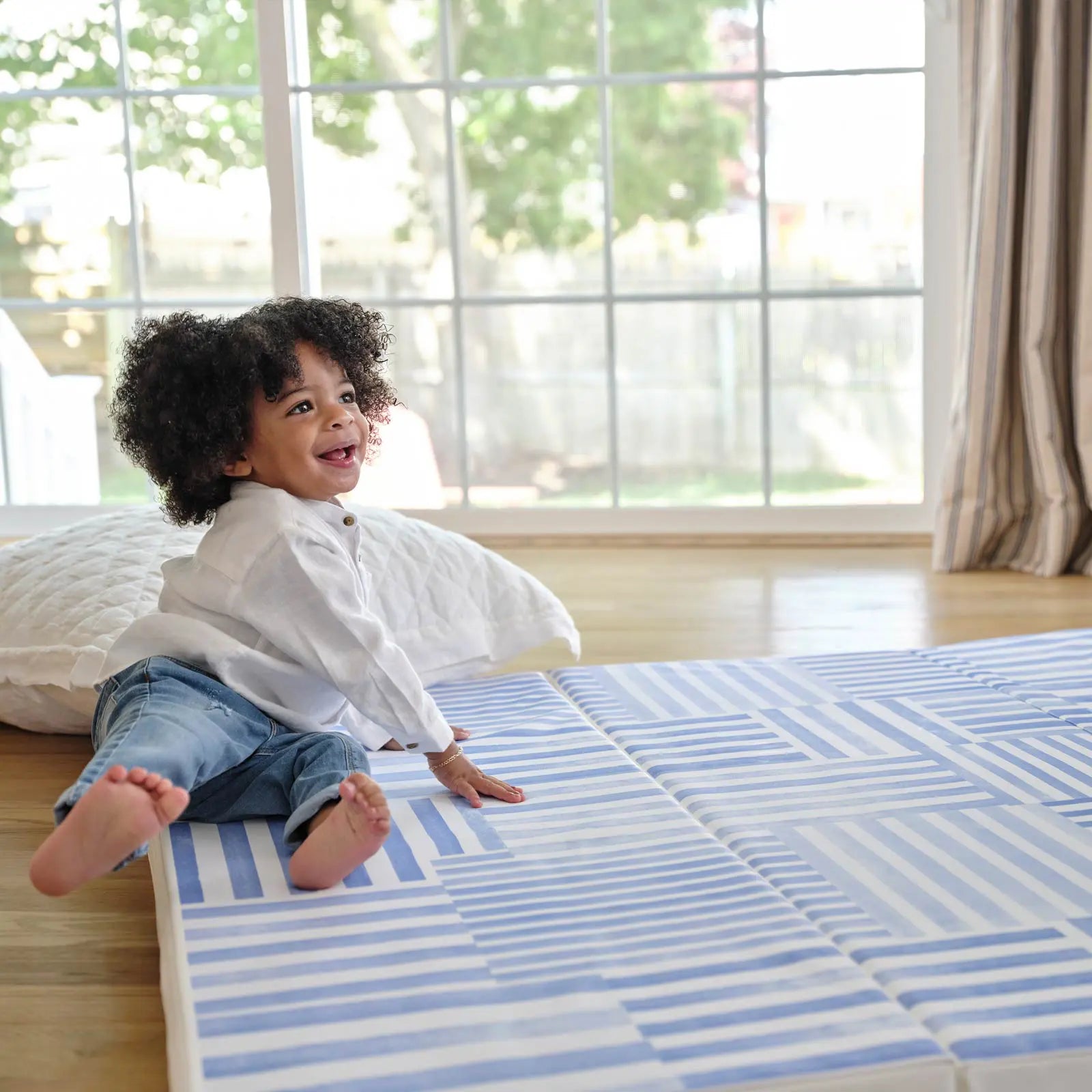 French blue and white inverted stripe tumbling mat with toddler smiling and laying down near the corner of the mat