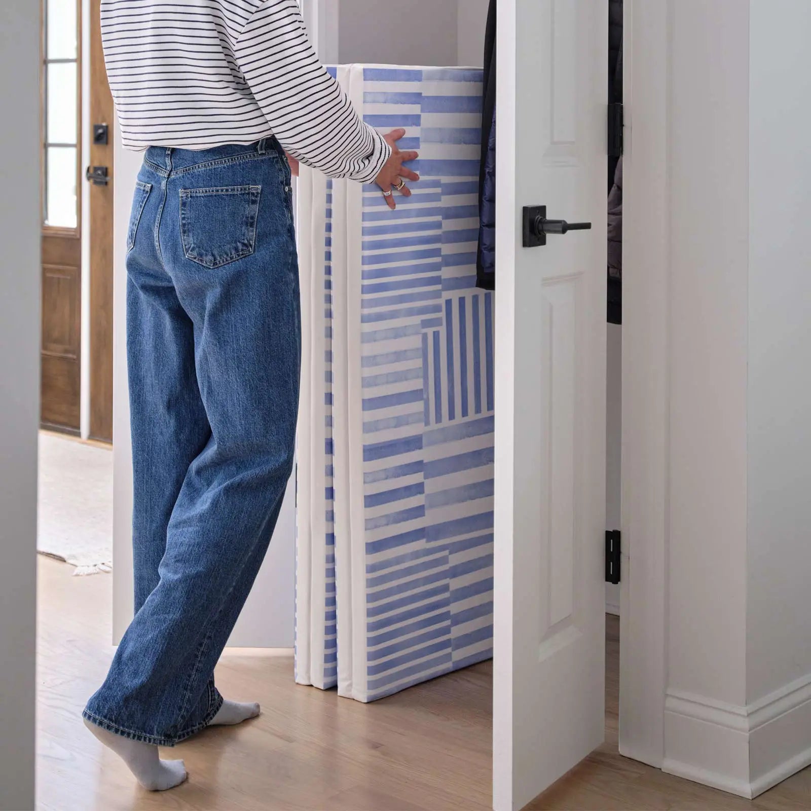 French blue and white inverted stripe tumbling mat shown folded with a woman putting it in a closet