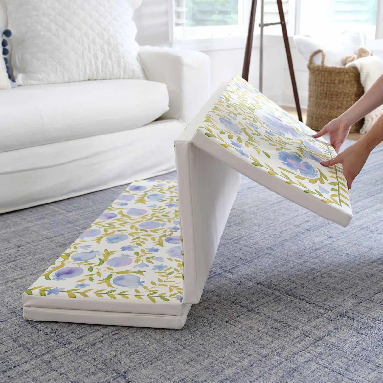 Bluebell blue green and white floral tumbling mat shown in living room with 2 panels folded up and the other 2 panels being folded by a womans hands