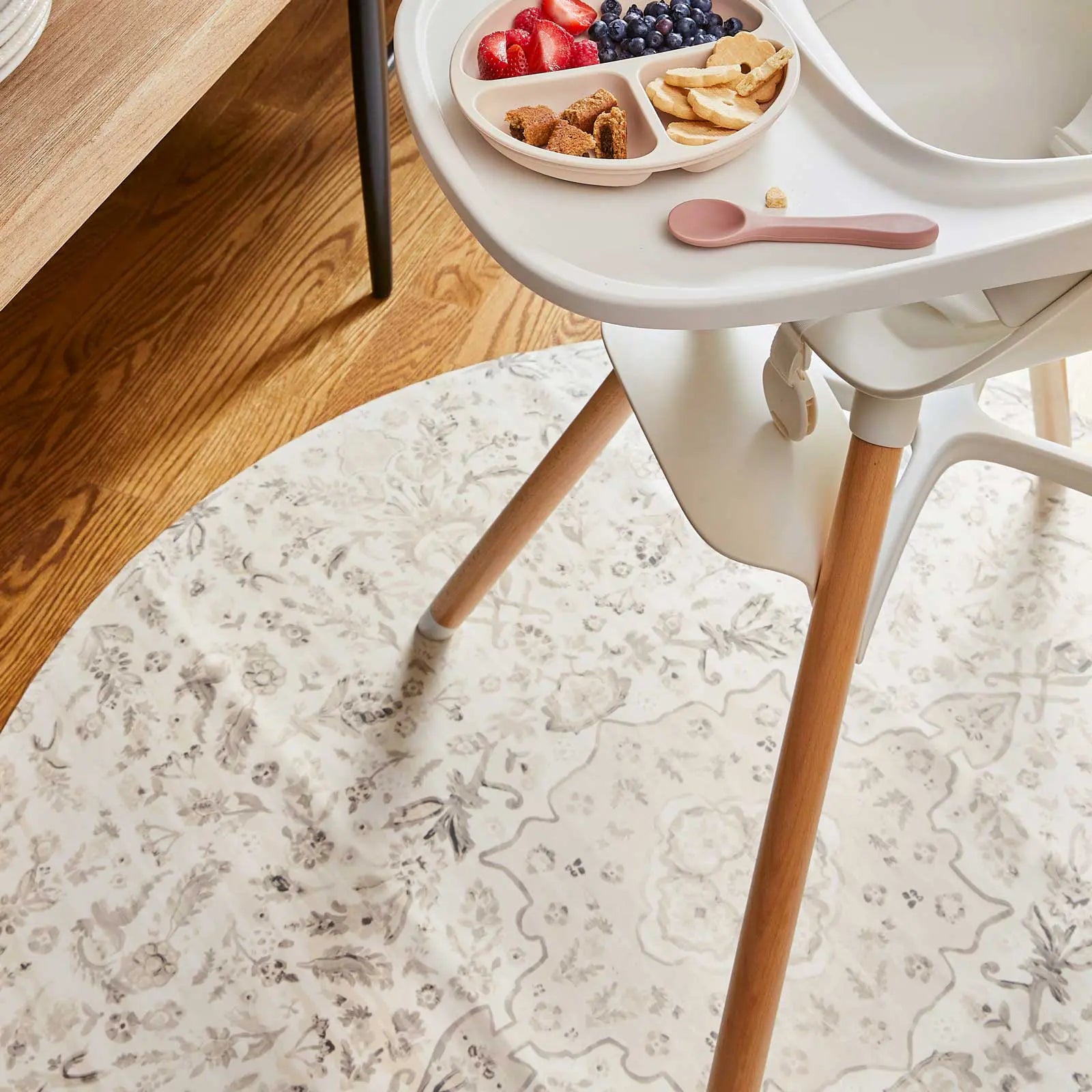 Emile latte neutral beige and gray vintage floral print high chair mat shown underneath a highchair with cookies and fruit on the tray
