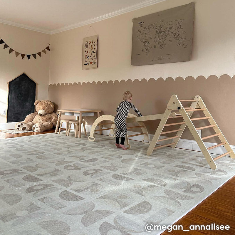 Luna sandstone neutral geometric print play mat shown in beige play room with toddler climbing on wooden toys