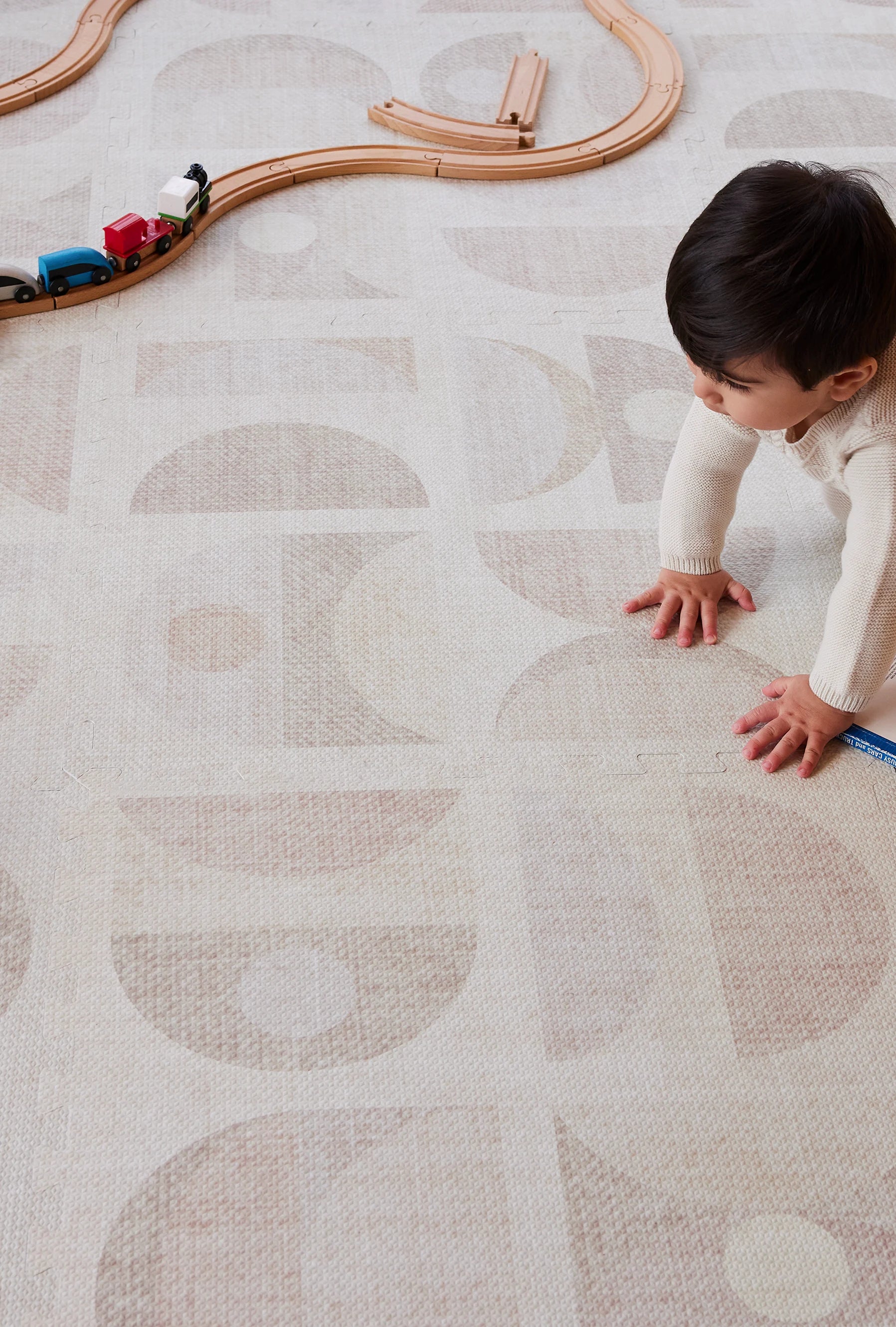 Luna sandstone play mat with baby boy playing crawling across the mat with wooden train tracks in the corner  