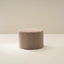 A light brown upholstered ottoman with a round shape placed on a white background.