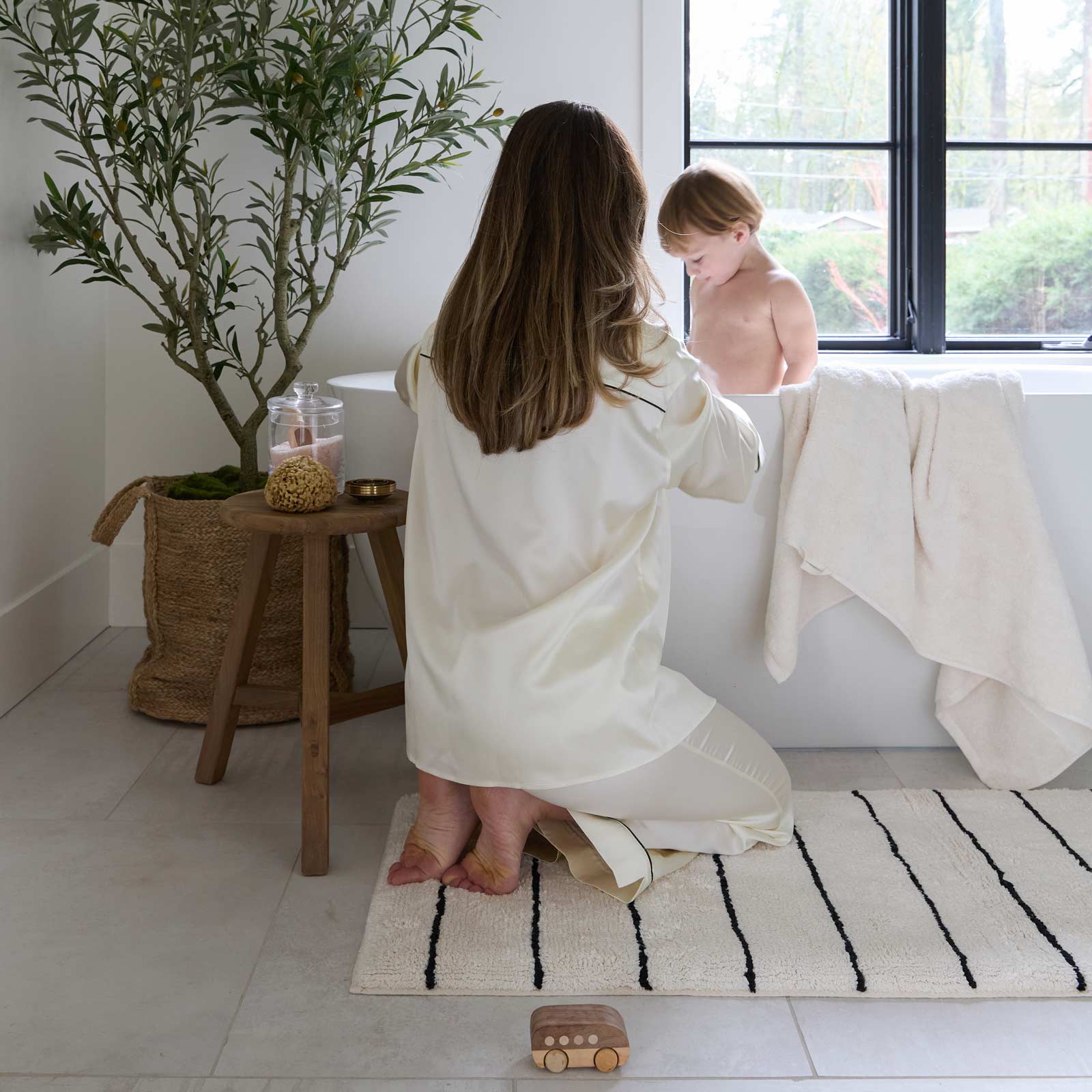 mom kneeling on house of noa bath mat for toddler bath time