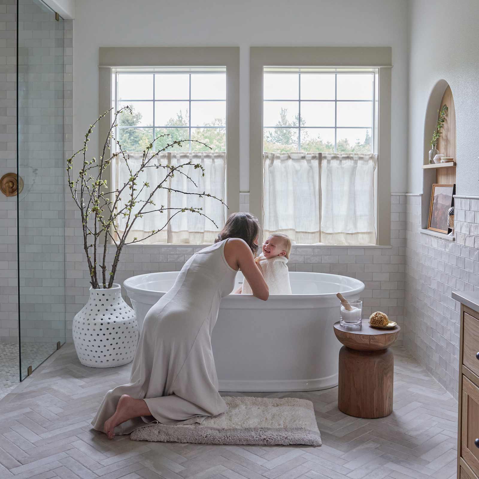 mom giving her baby a bath kneeling on a house of noa bath mat