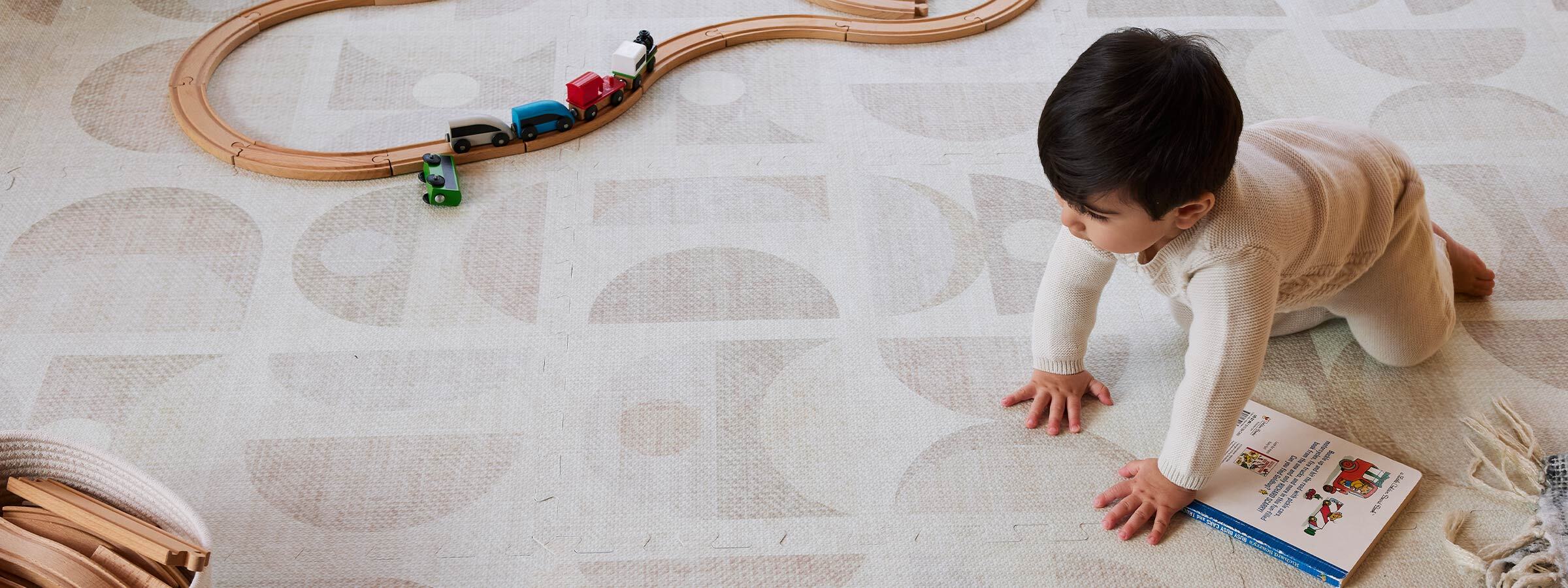 Luna sandstone neutral geometric print play mat with wooden train set, books, and baby boy crawling across the mat