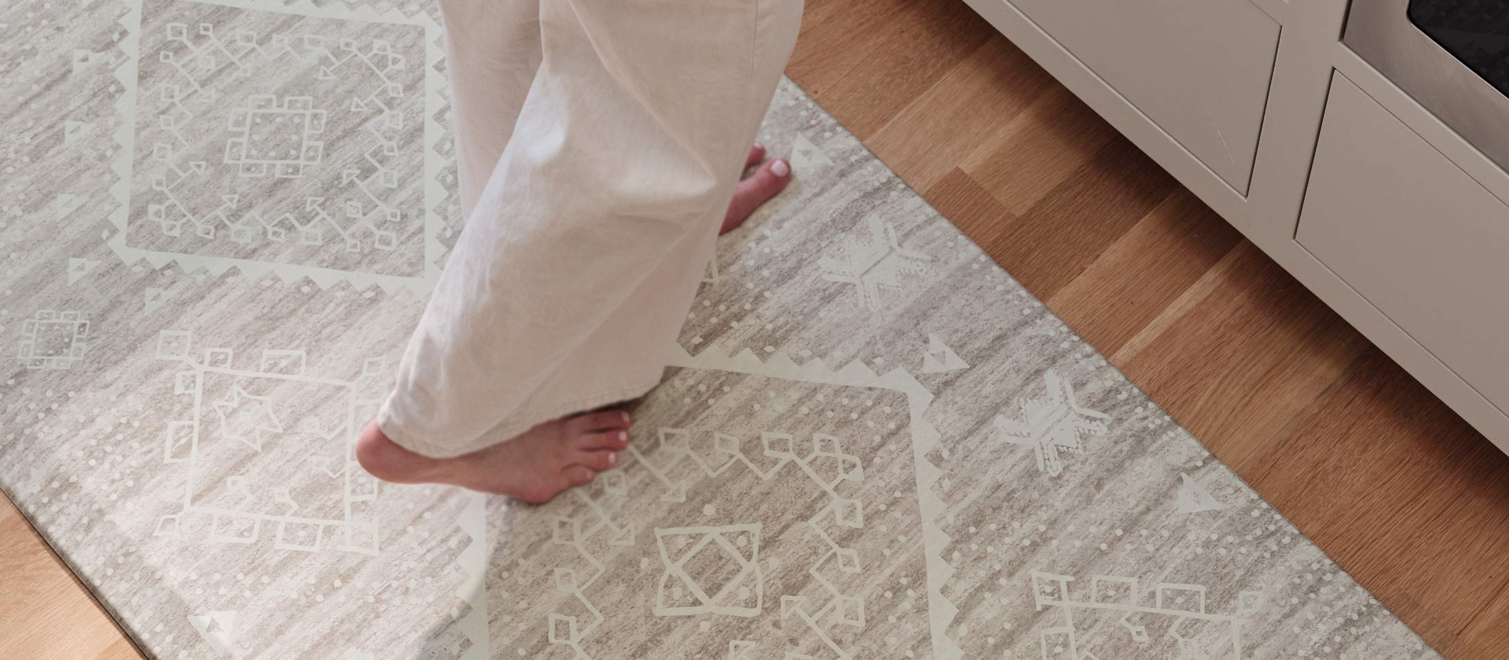 Fawn brown neutral animal print standing mat shown with woman's feet in slippers and babies feet standing on the mat at floor level