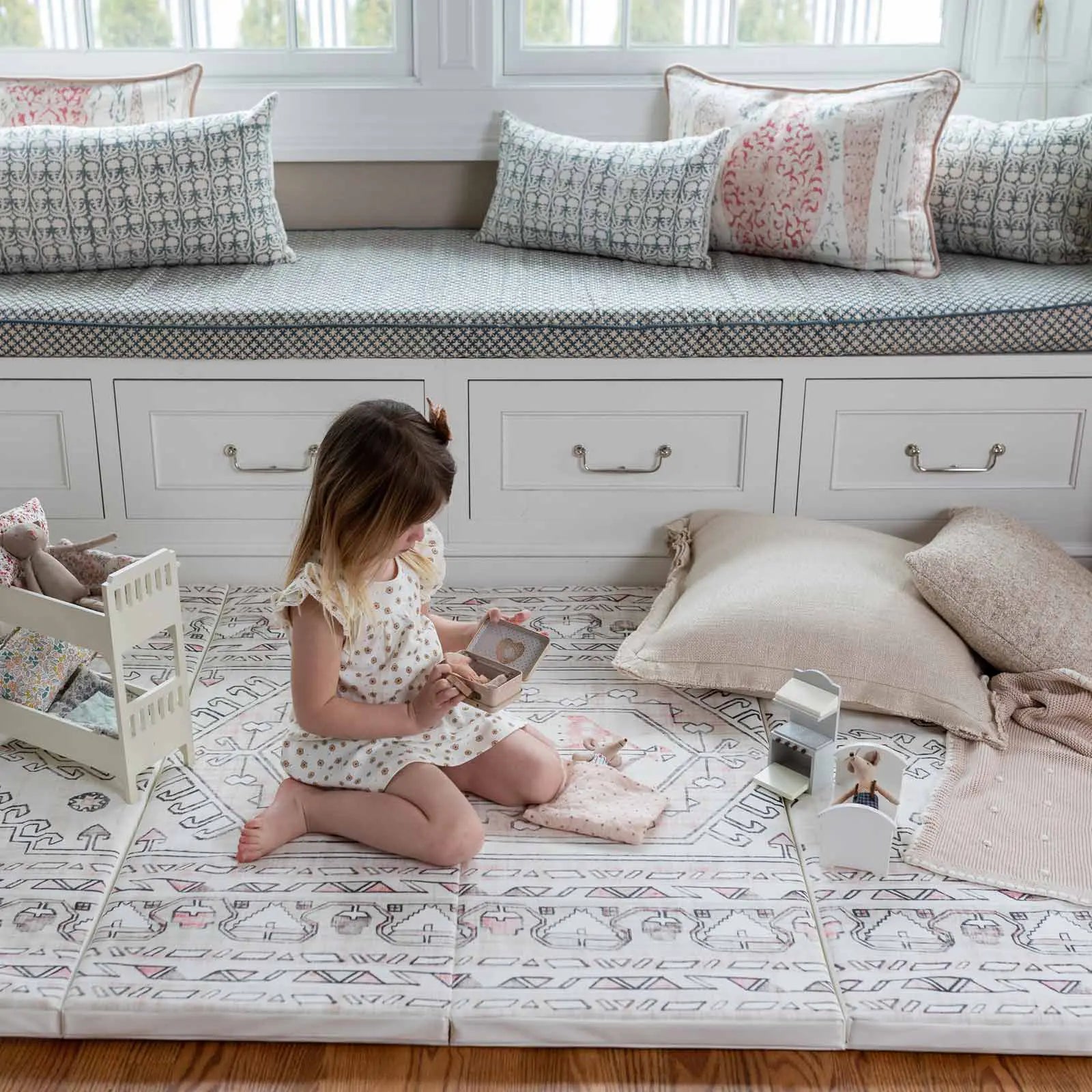 Aryla Shifting Sands cream and pink boho tumbling mat shown in front of the window seat with little girl sitting with pillow and her toys playing