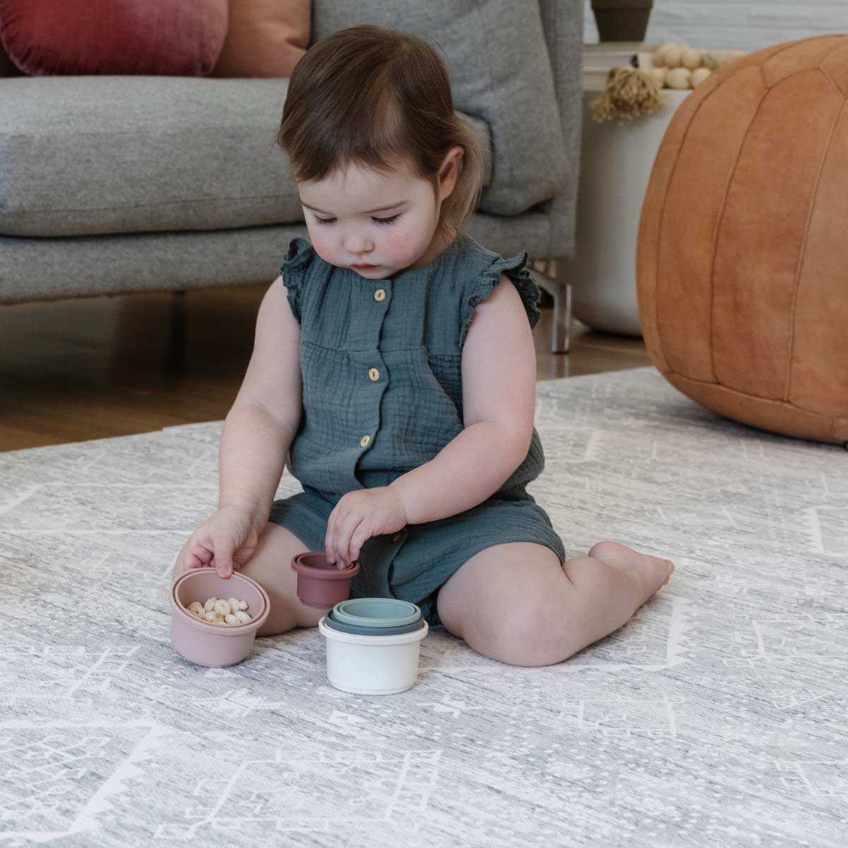 Little Nomad baby play mat in Ula Gray neutral boho print. Shown in living room with baby playing with toys.