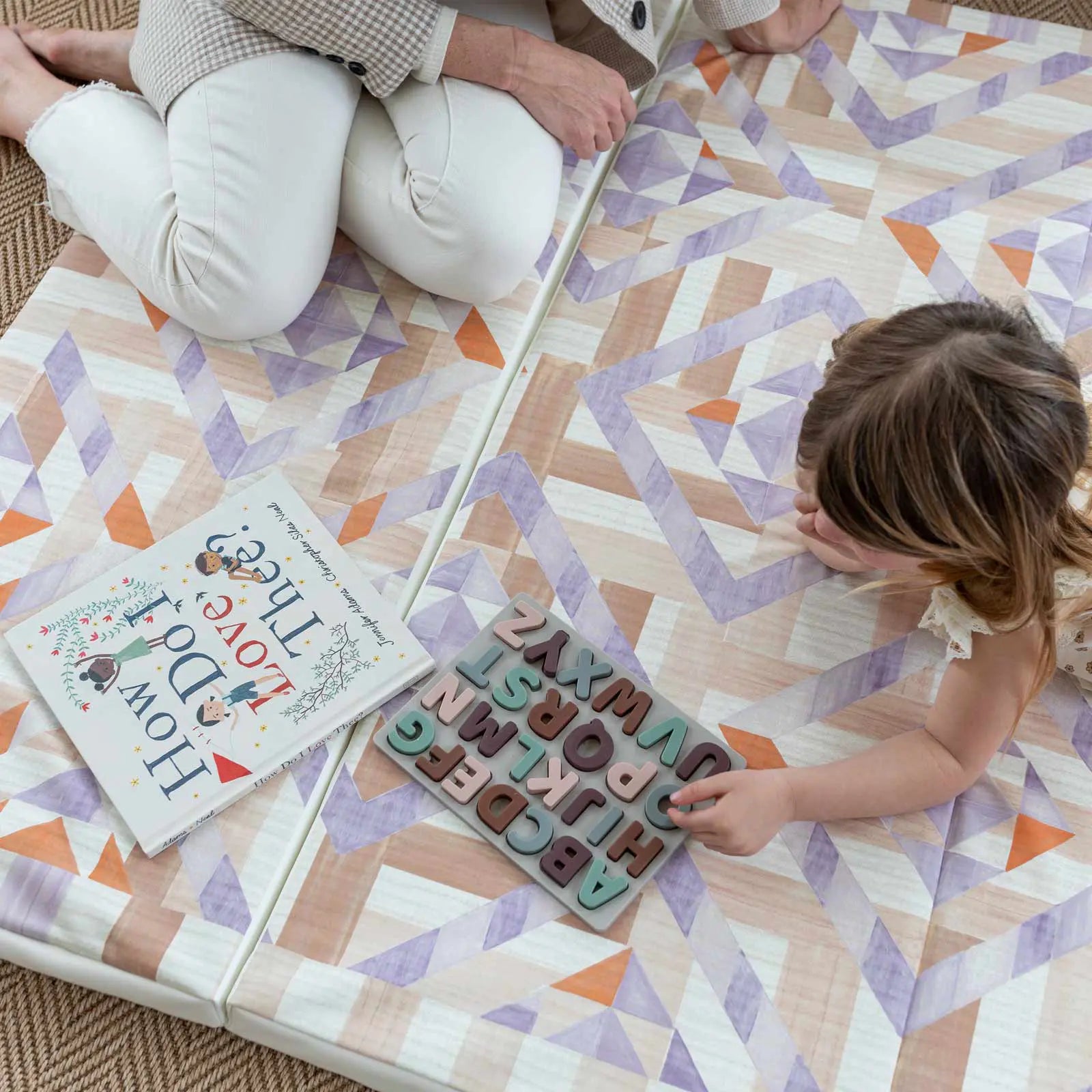 Marigold pink, purple, and orange quilt pattern tumbling mat, shown from above with mom and little girl playing with wooden alphabet puzzle.