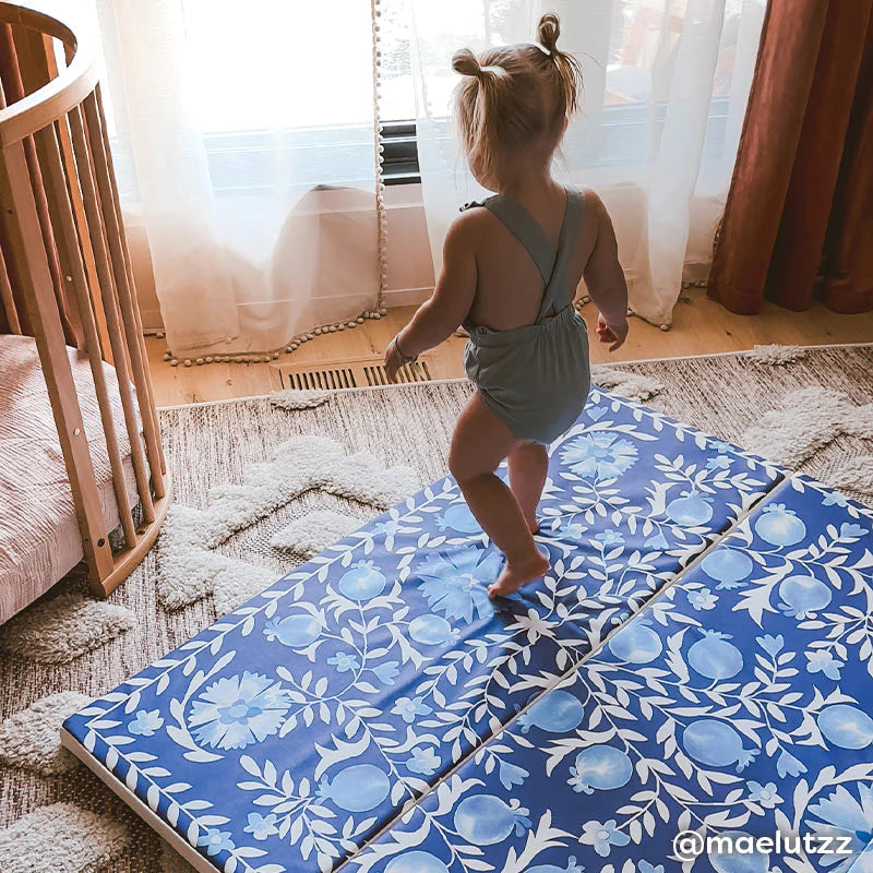 suzette deep sea navy and blue floral tumbling mat shown in nursery with toddler girl walking across the mat. @maelutzz written in lower right hand corner.