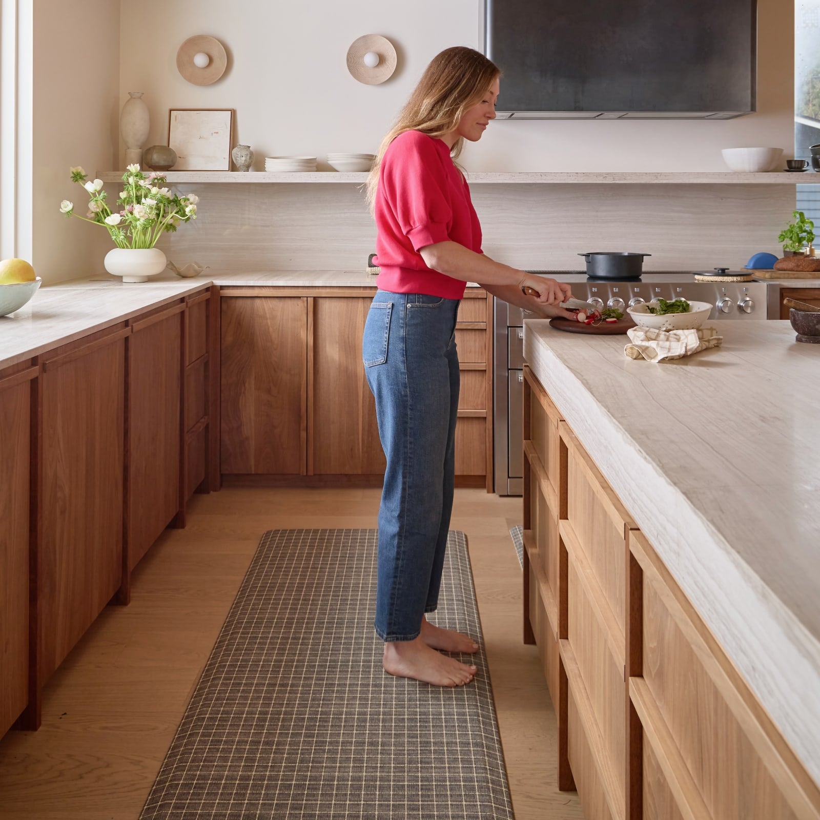 Woman in a kitchen preparing food on a countertop standing on a grid pattern kitchen mat.