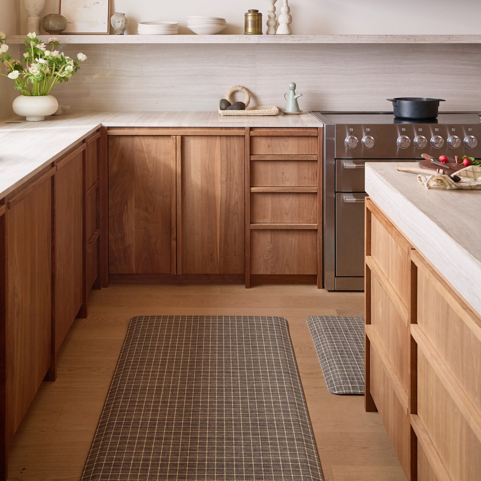 Modern kitchen with wooden cabinets, stainless steel appliances, and white countertops and two grid pattern kitchen mats on the floor.