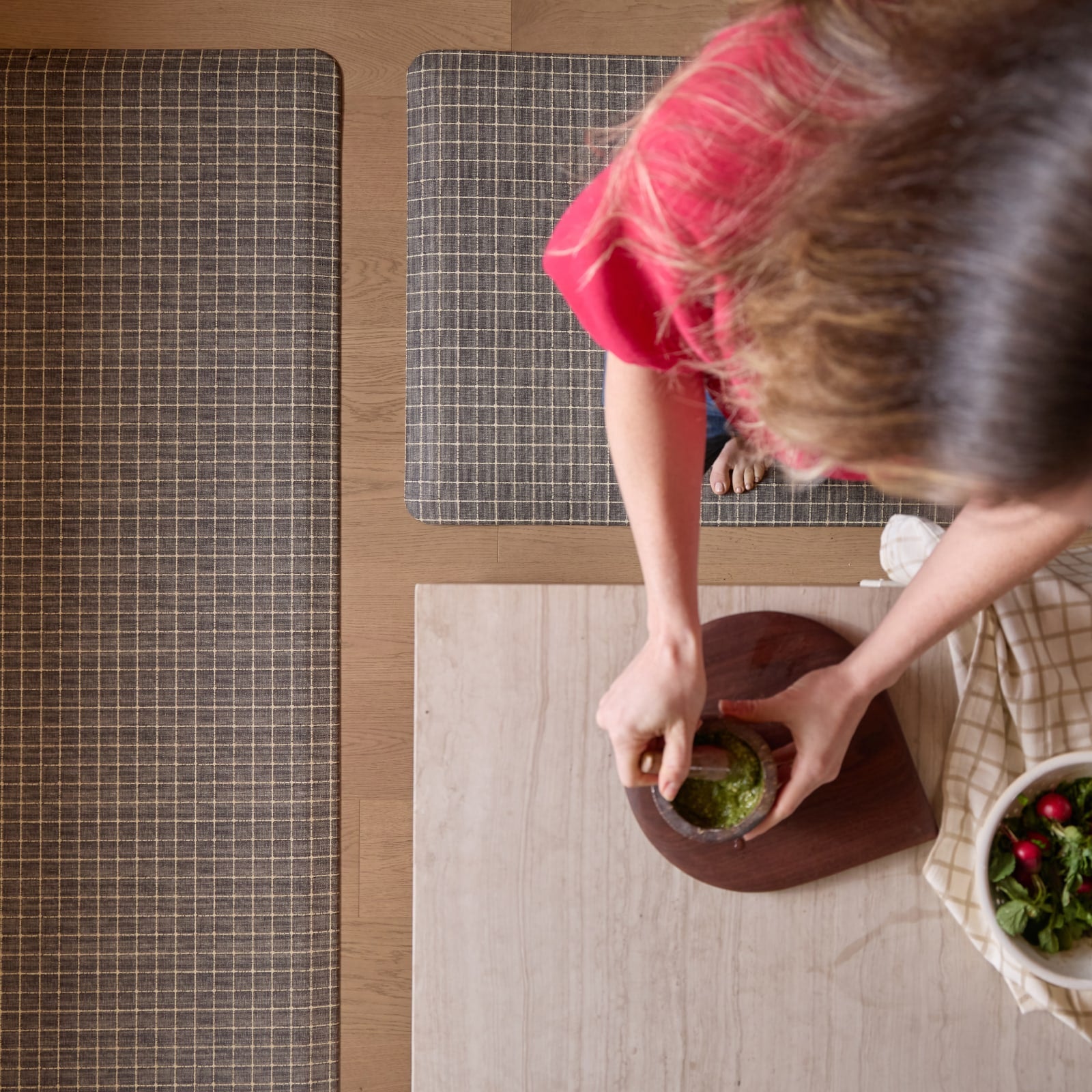 Person preparing food on a wooden surface with standing on a grid patterned mat.