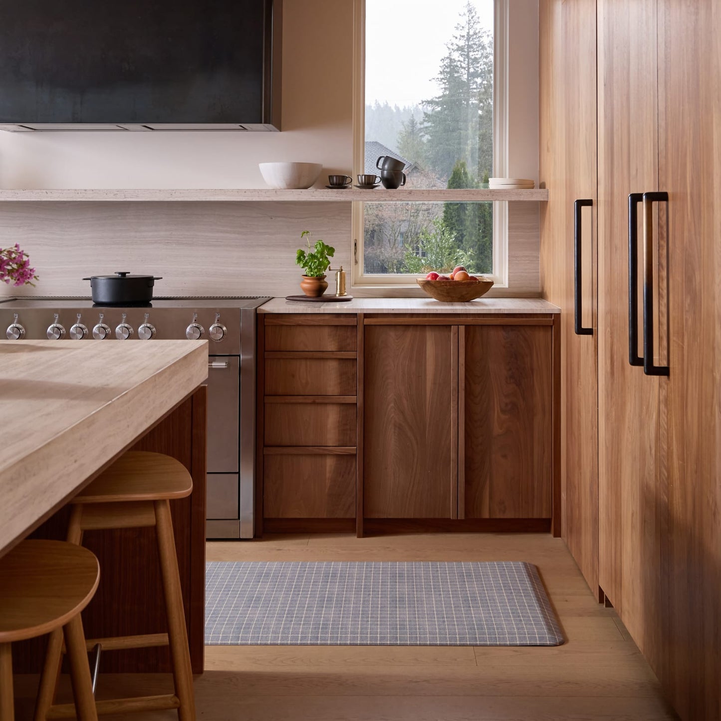 Modern kitchen with wooden cabinets, a grid pattern kitchen mat, and a view of trees outside the window.