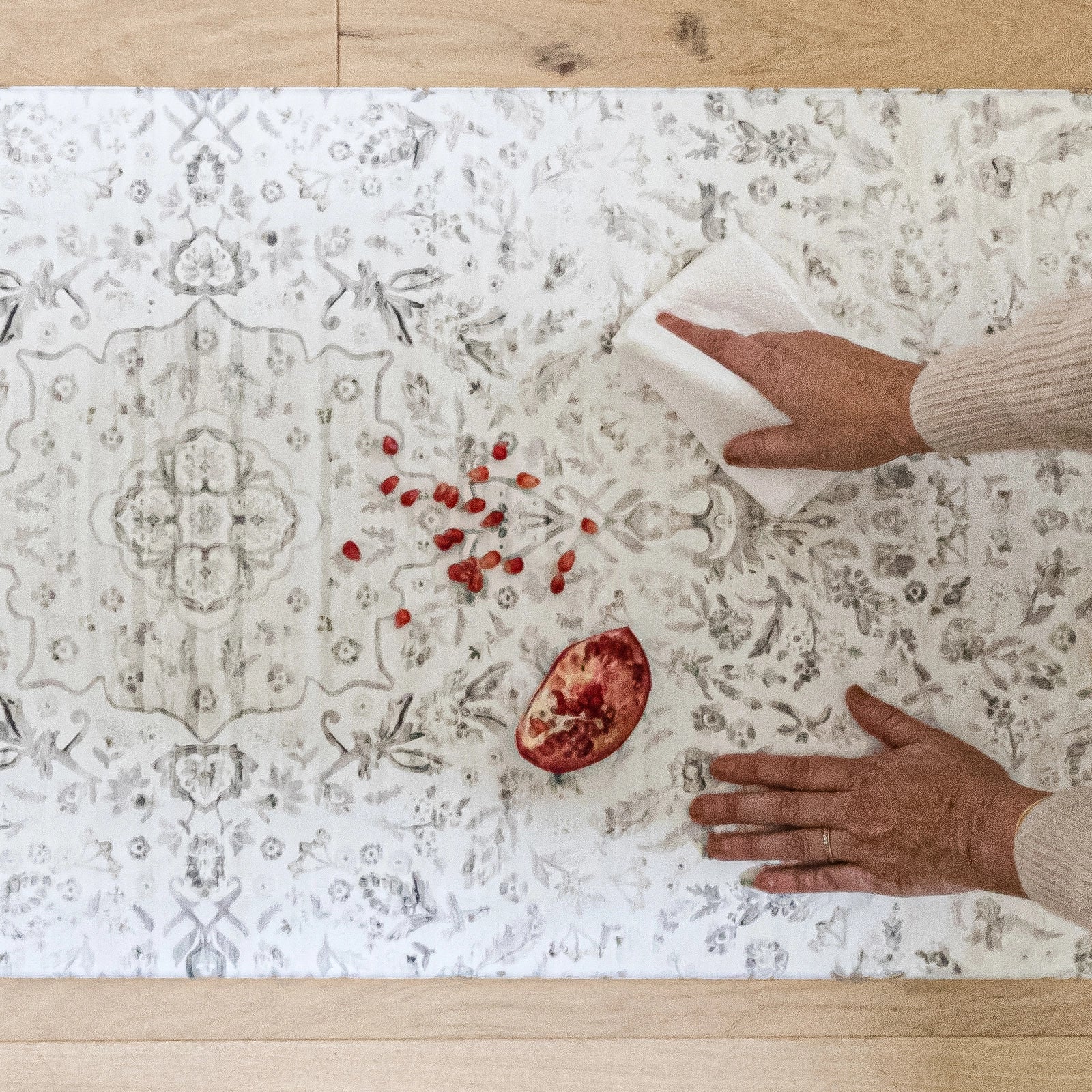Emile latte beige and gray floral boho kitchen mat shown shown with woman's hand wiping up spilled pomegranate