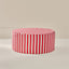A round pouf ottoman with a red and white vertical stripe pattern, shown on a neutral beige background.