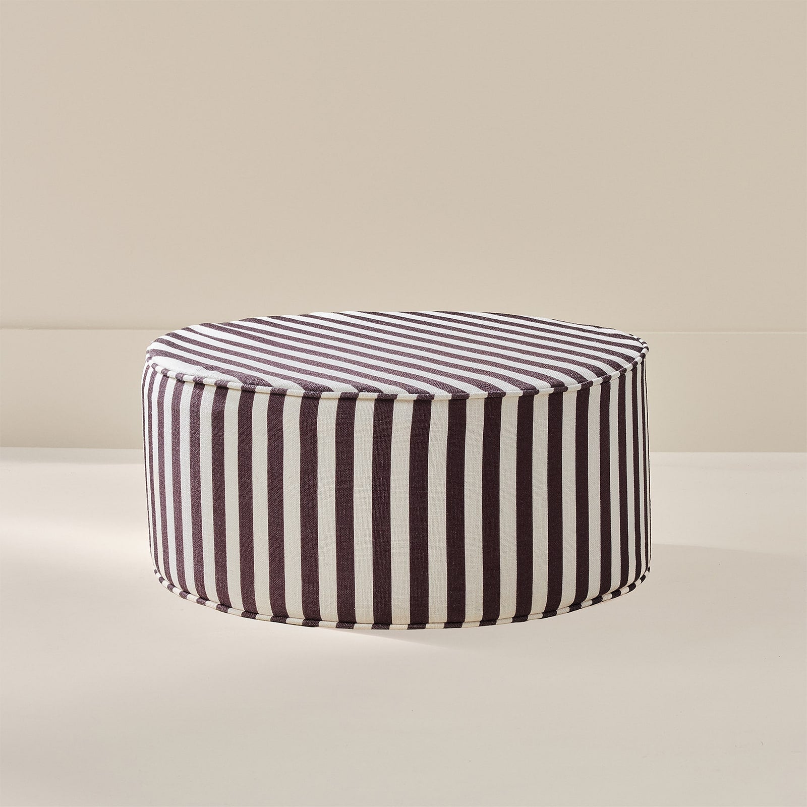 A round upholstered ottoman with vertical dark brown and white stripes, shown on a clean beige studio background.