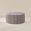 A round upholstered ottoman with vertical dark brown and white stripes, shown on a clean beige studio background.