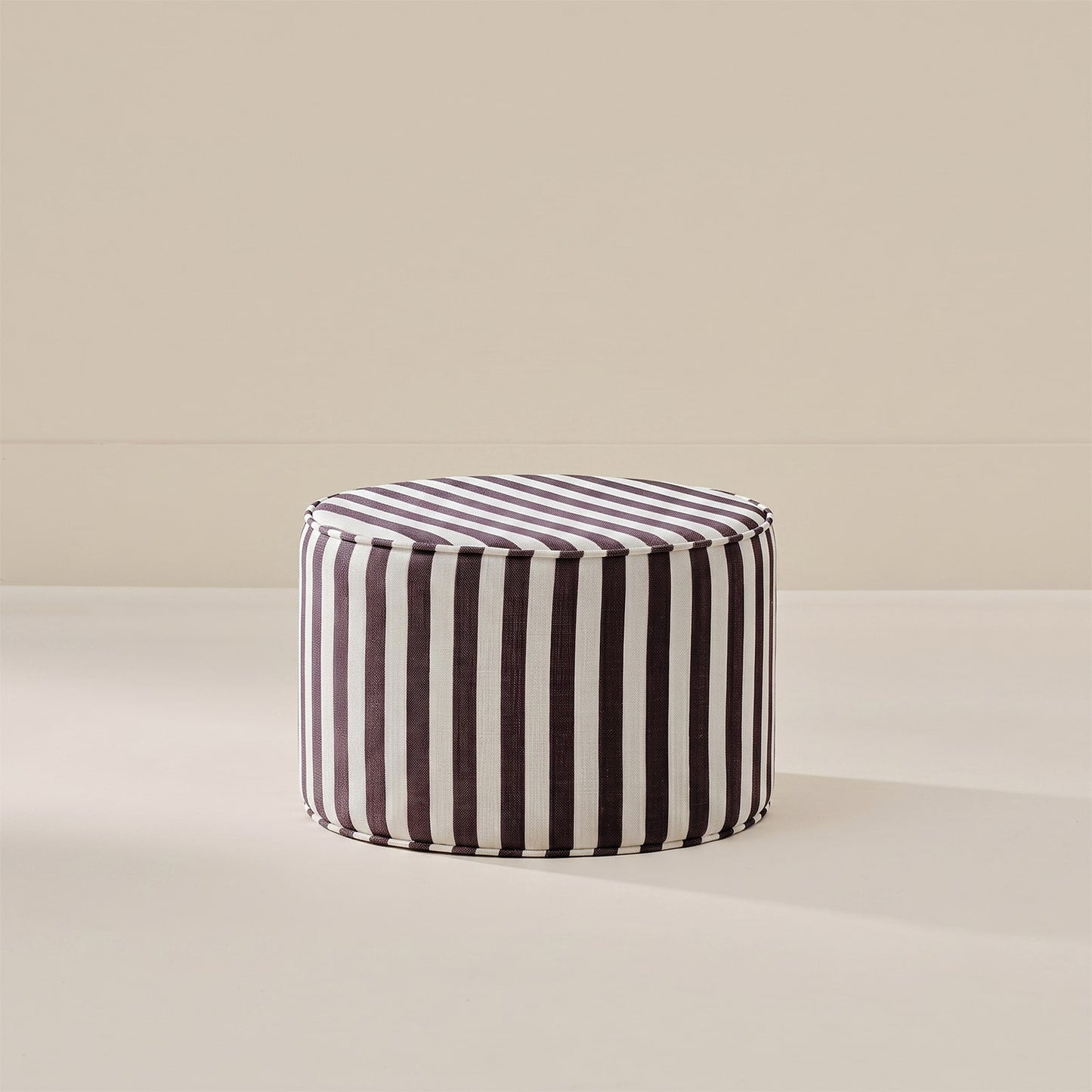 A round pouf ottoman with vertical black and white stripes, set against a minimalist beige background.