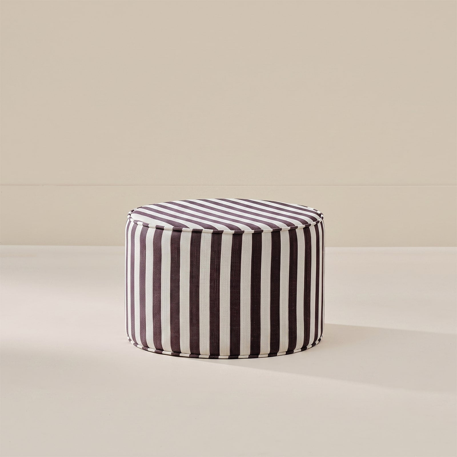 A round pouf ottoman with vertical black and white stripes, set against a minimalist beige background.