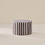 A round pouf ottoman with vertical black and white stripes, set against a minimalist beige background.