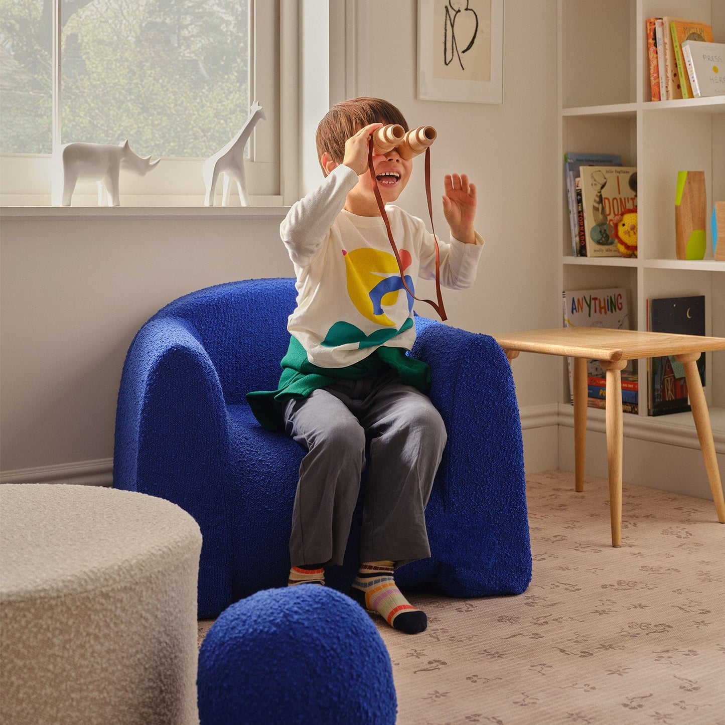 Child playing with a toy in a blue chair in a room with books and decor.