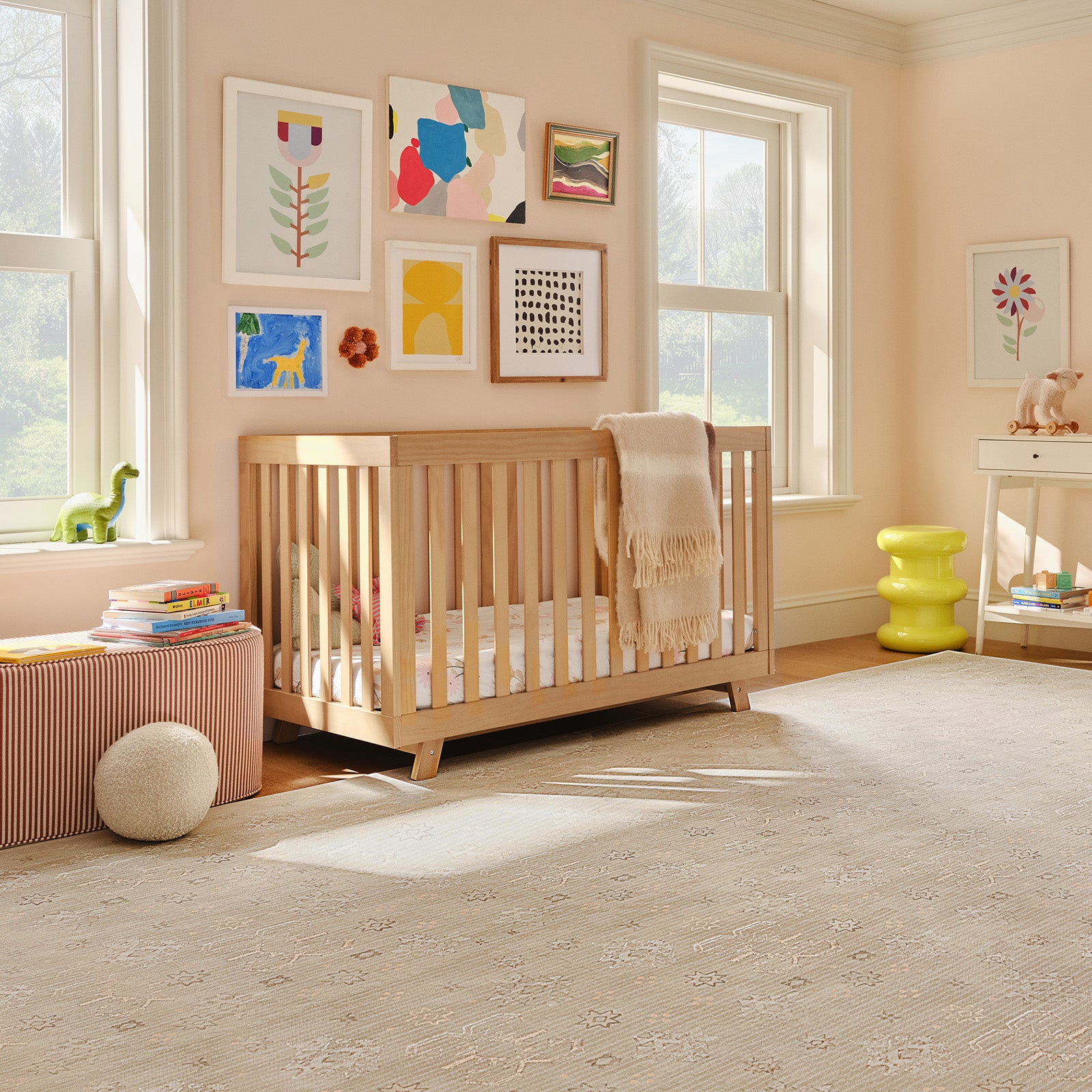 Nursery room with wooden crib, colorful artwork on the wall, beige play mat, and toys around.
