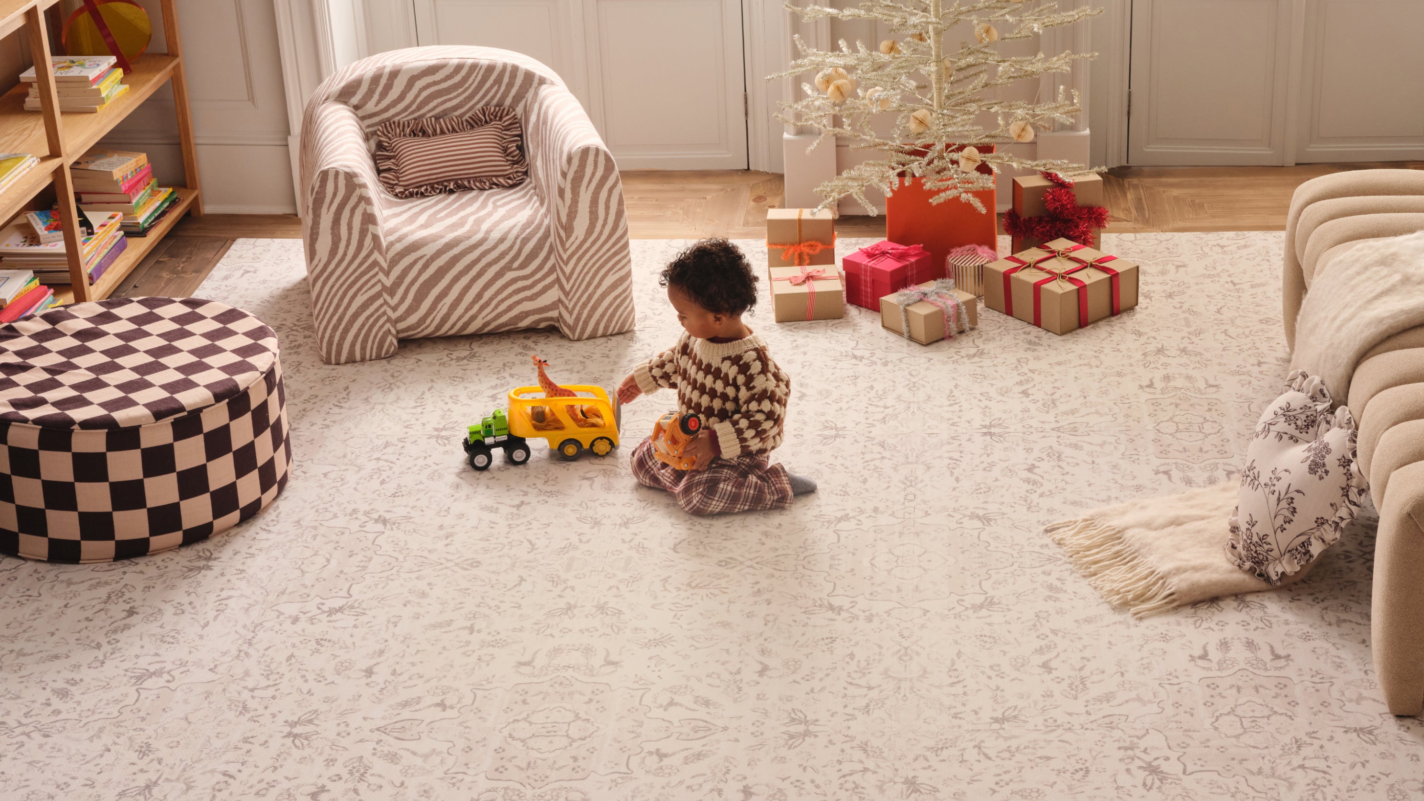 Child playing with toys on a neutral play mat in a living room with an ottoman and play chair.