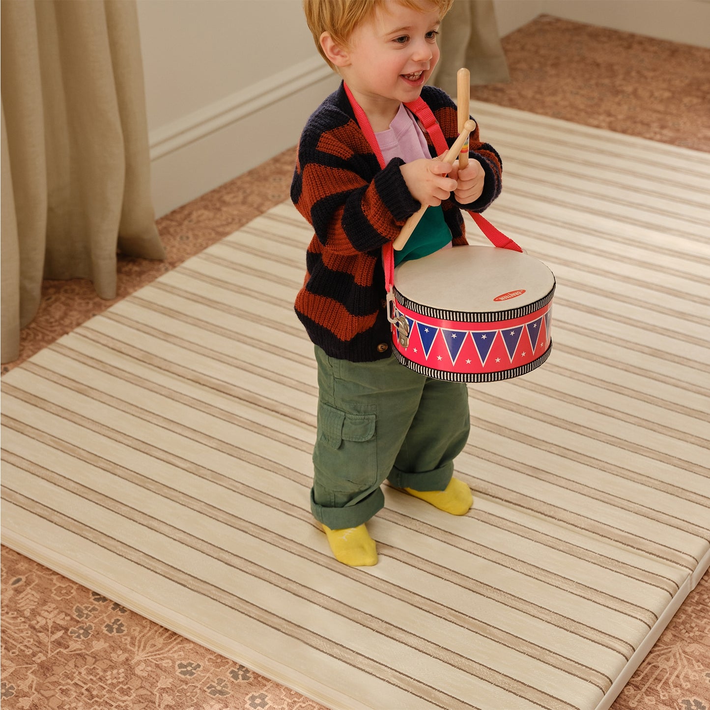 Child playing with a drum on a striped play mat
