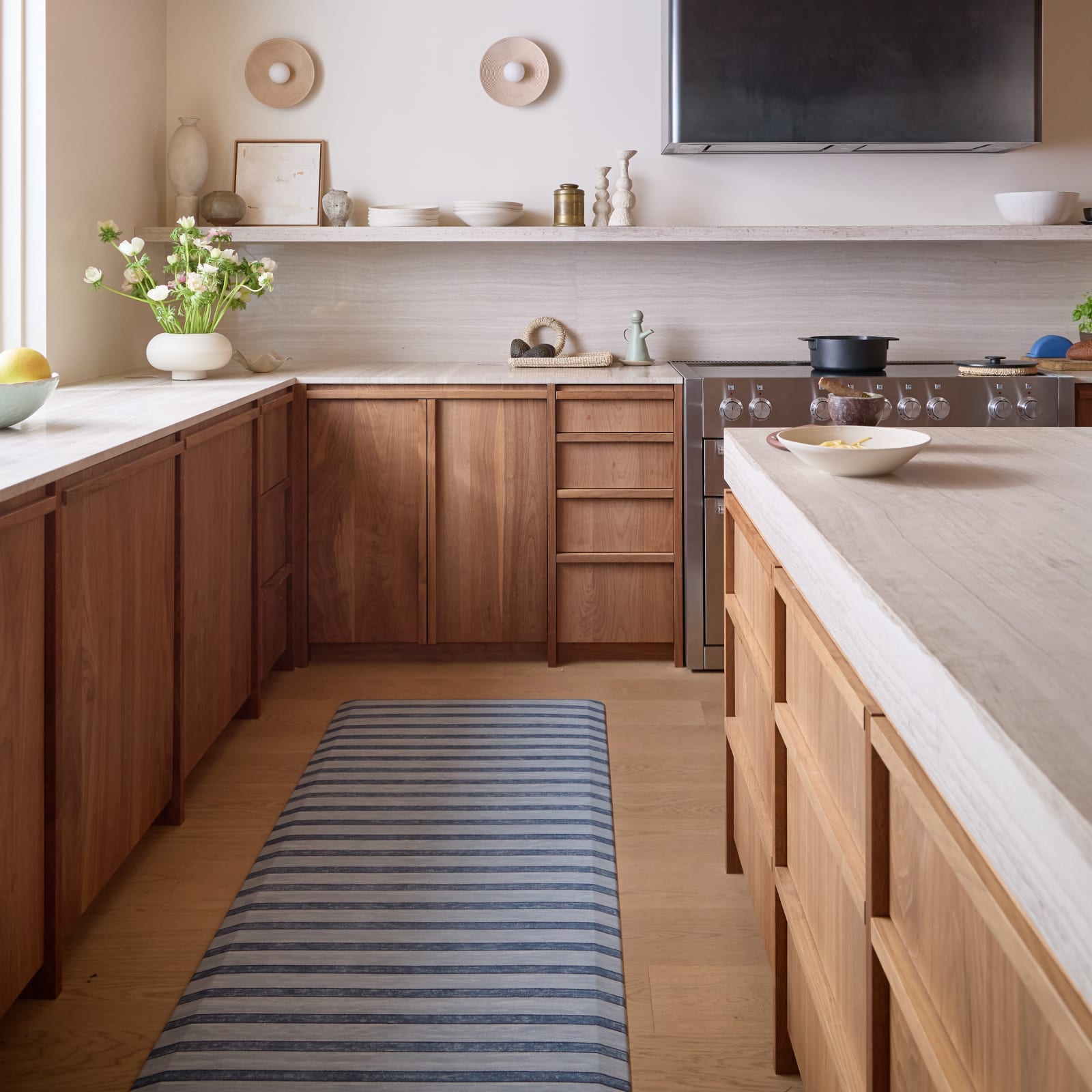 Modern kitchen with wooden cabinets, marble countertops, and a striped kitchen mat on the floor.
