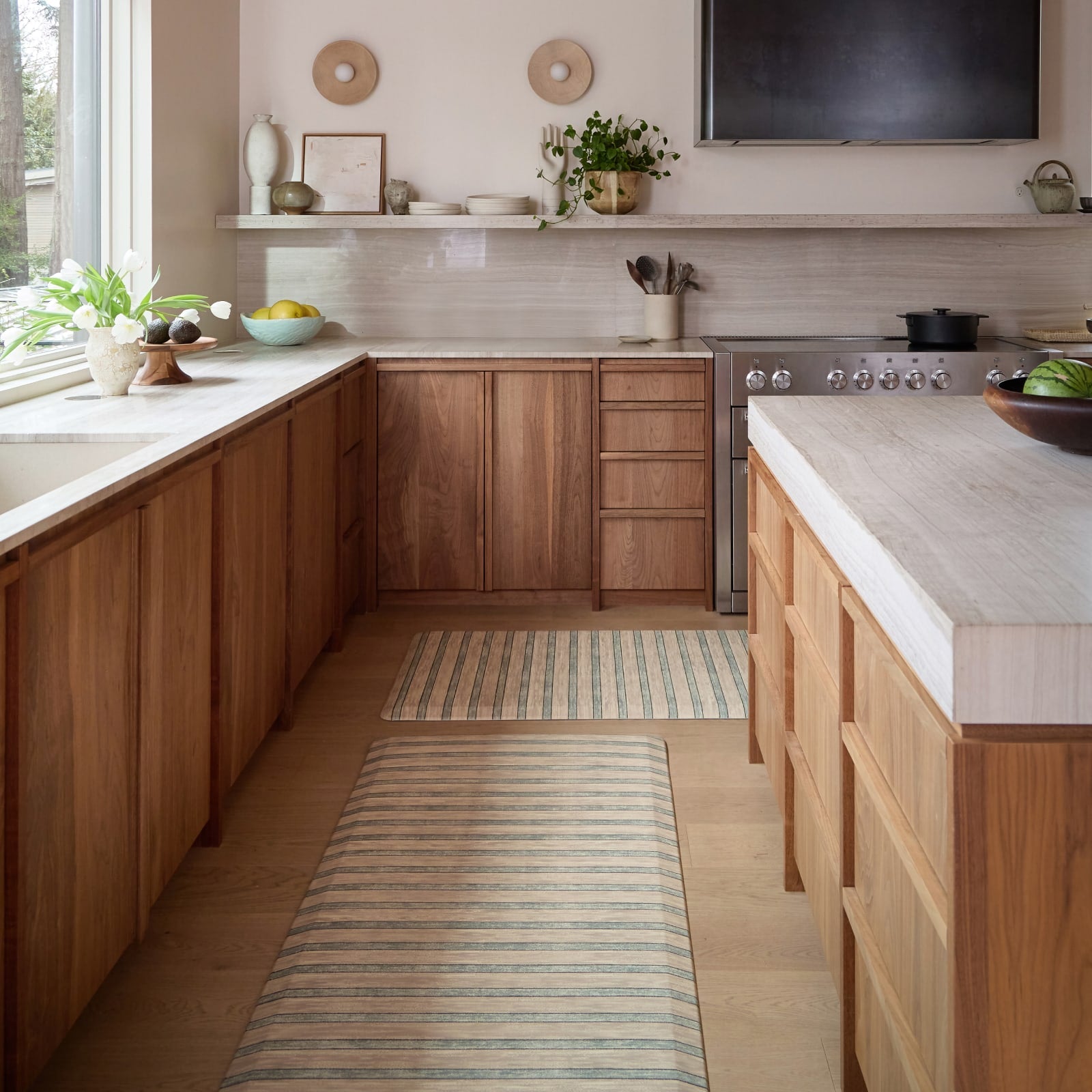 Modern kitchen with wooden cabinets, white countertops, and a striped kitchen mat on the floor.