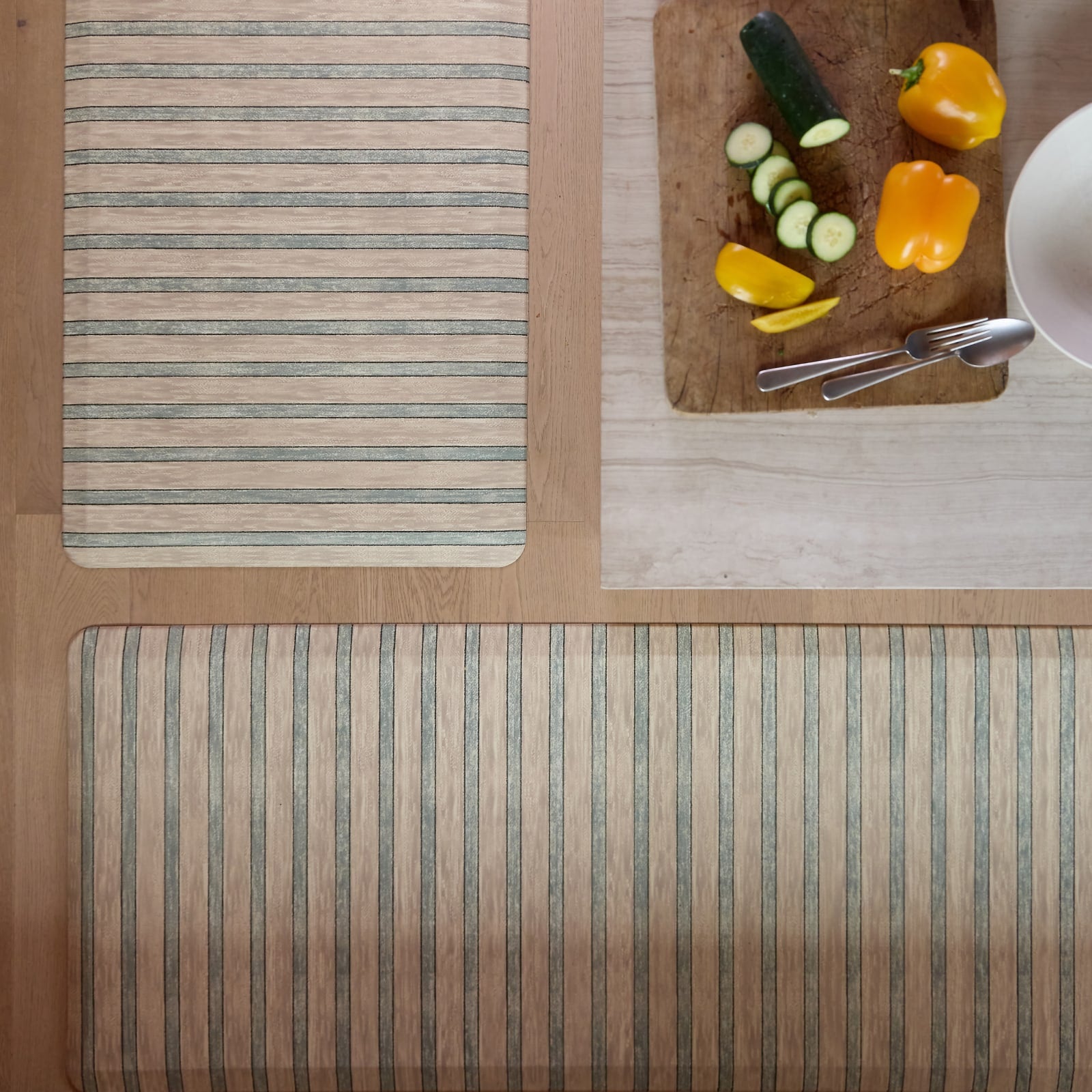 Striped kitchen mats on a wooden floor with vegetables and cutlery on the counter nearby.