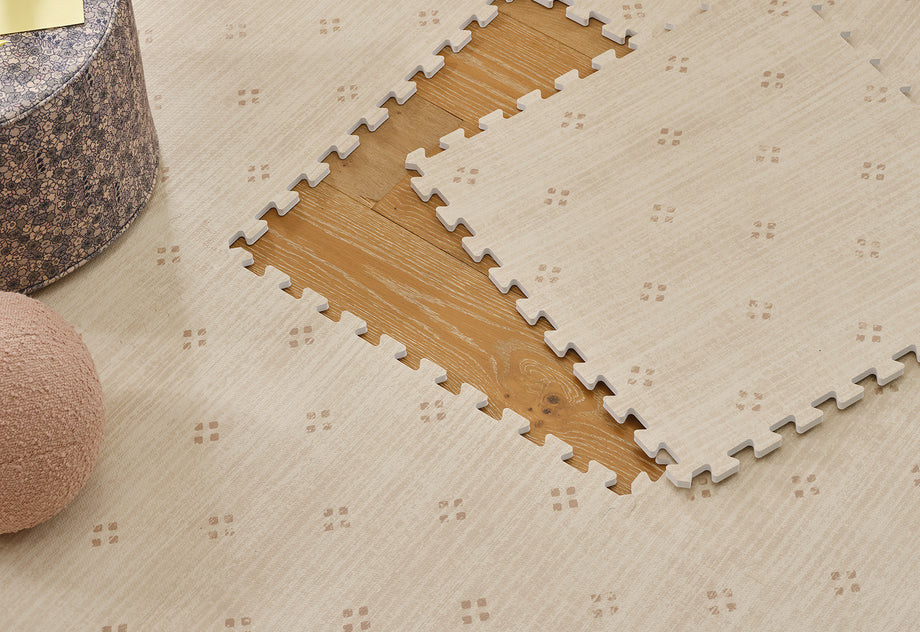 Beige interlocking foam mat with 1 tile lifted to show light wood floor underneath