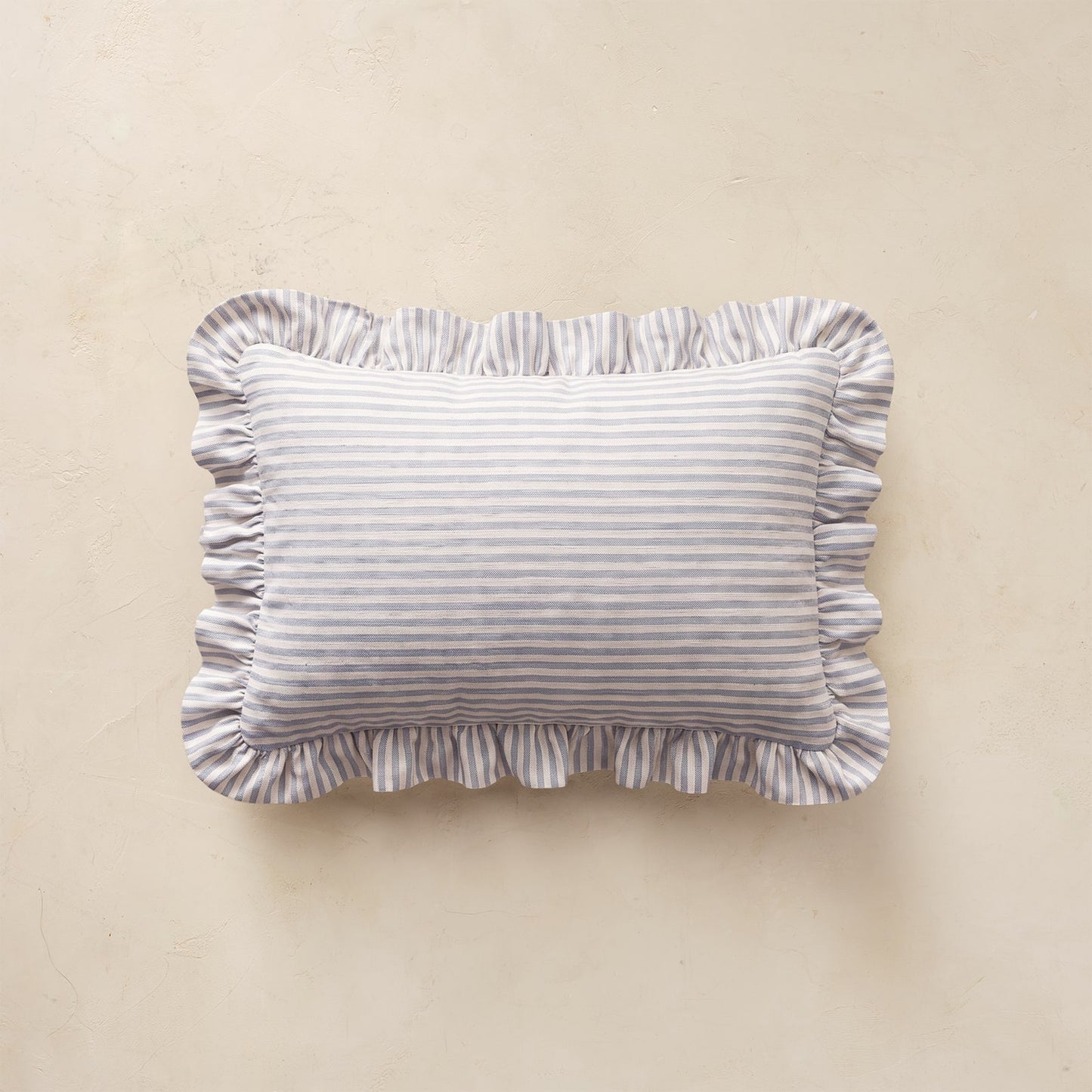 A rectangular throw pillow with ruffled edges, featuring a fine horizontal stripe pattern in light blue and white, displayed against a neutral beige background.