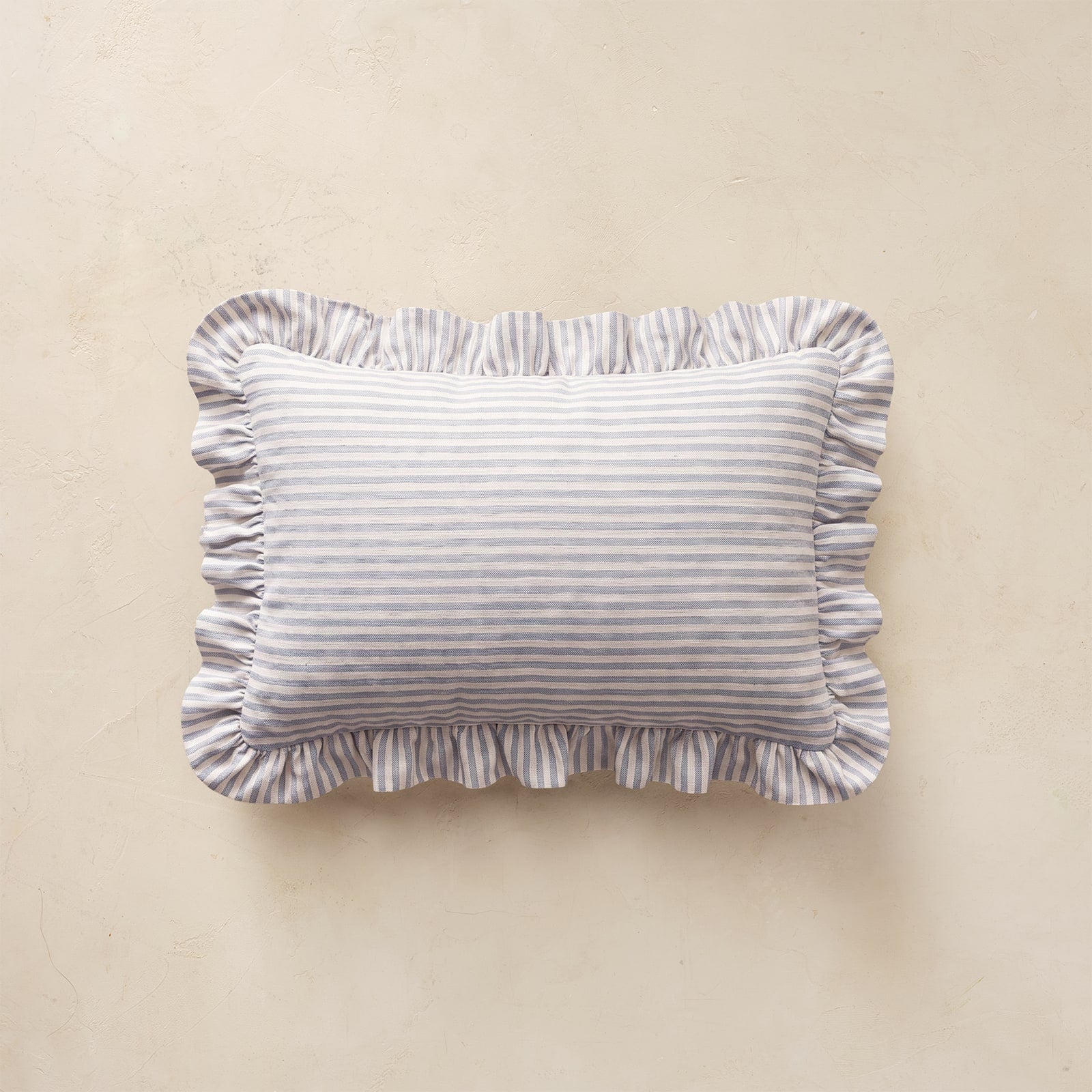 A rectangular throw pillow with ruffled edges, featuring a fine horizontal stripe pattern in light blue and white, displayed against a neutral beige background.