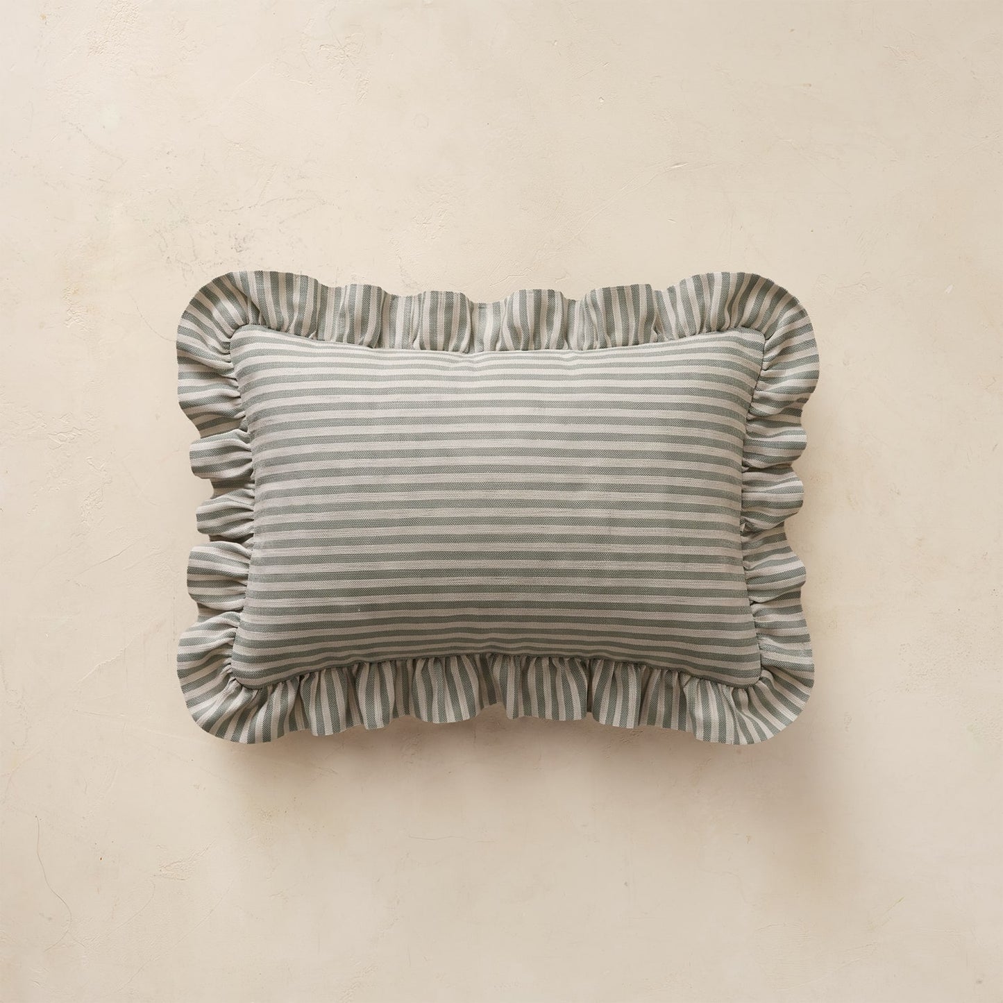 A rectangular throw pillow with ruffled edges, featuring a light green horizontal stripe pattern, displayed against a textured beige background.