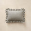 A rectangular throw pillow with ruffled edges, featuring a light green horizontal stripe pattern, displayed against a textured beige background.