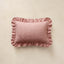 A rectangular decorative pillow with ruffled edges, featuring a dusty pink  horizontal stripe pattern, displayed against a textured beige background.